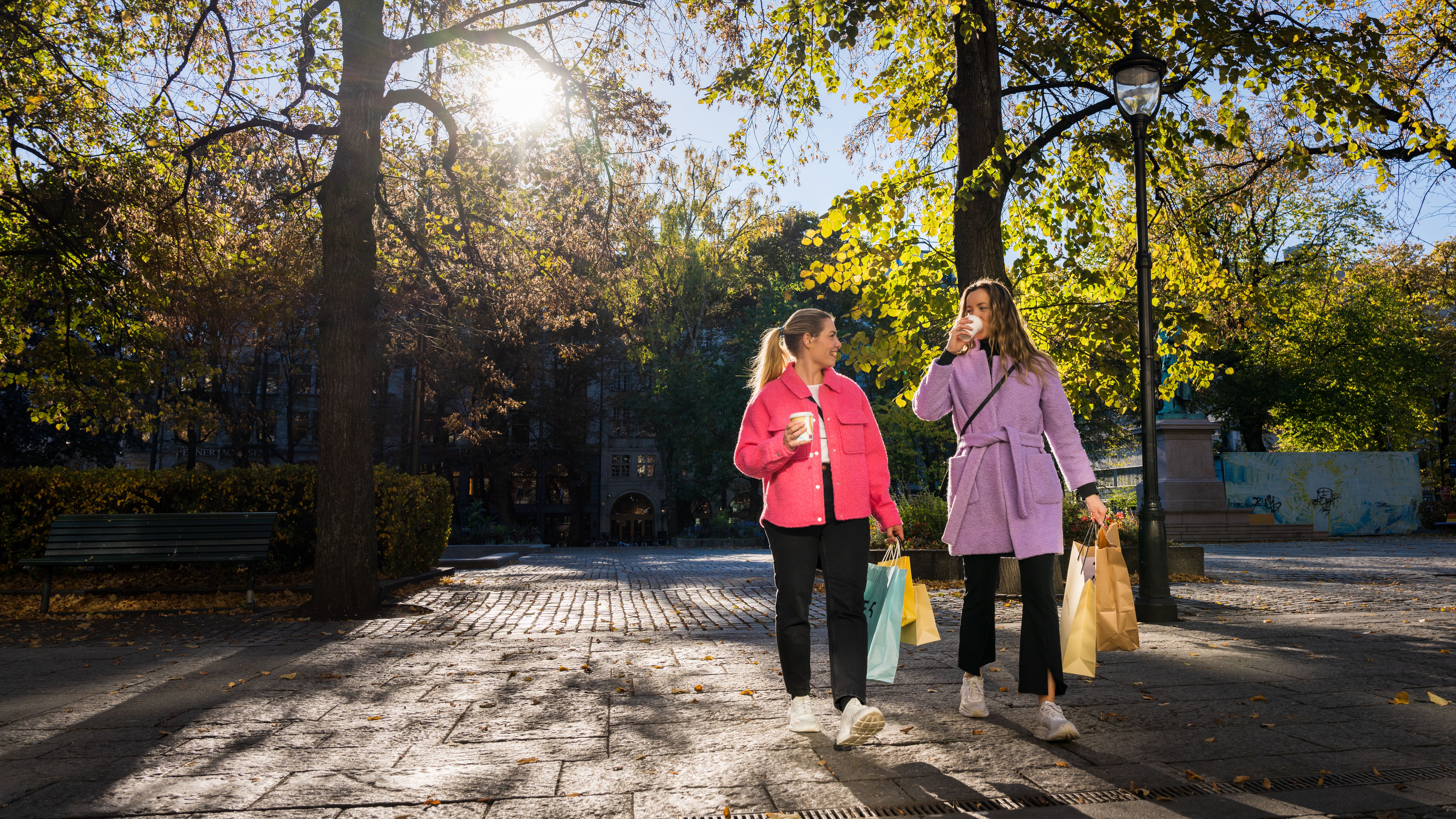 Two girls are laughing and drinking a coffee on the go in the shopping street Karl Johan in Oslo