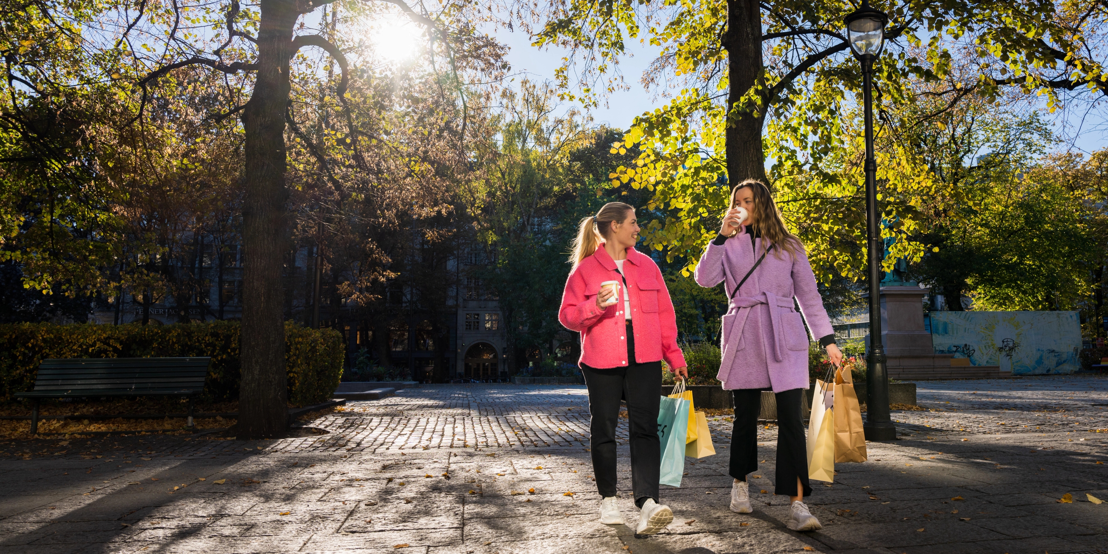Two girls are laughing and drinking a coffee on the go in the shopping street Karl Johan in Oslo