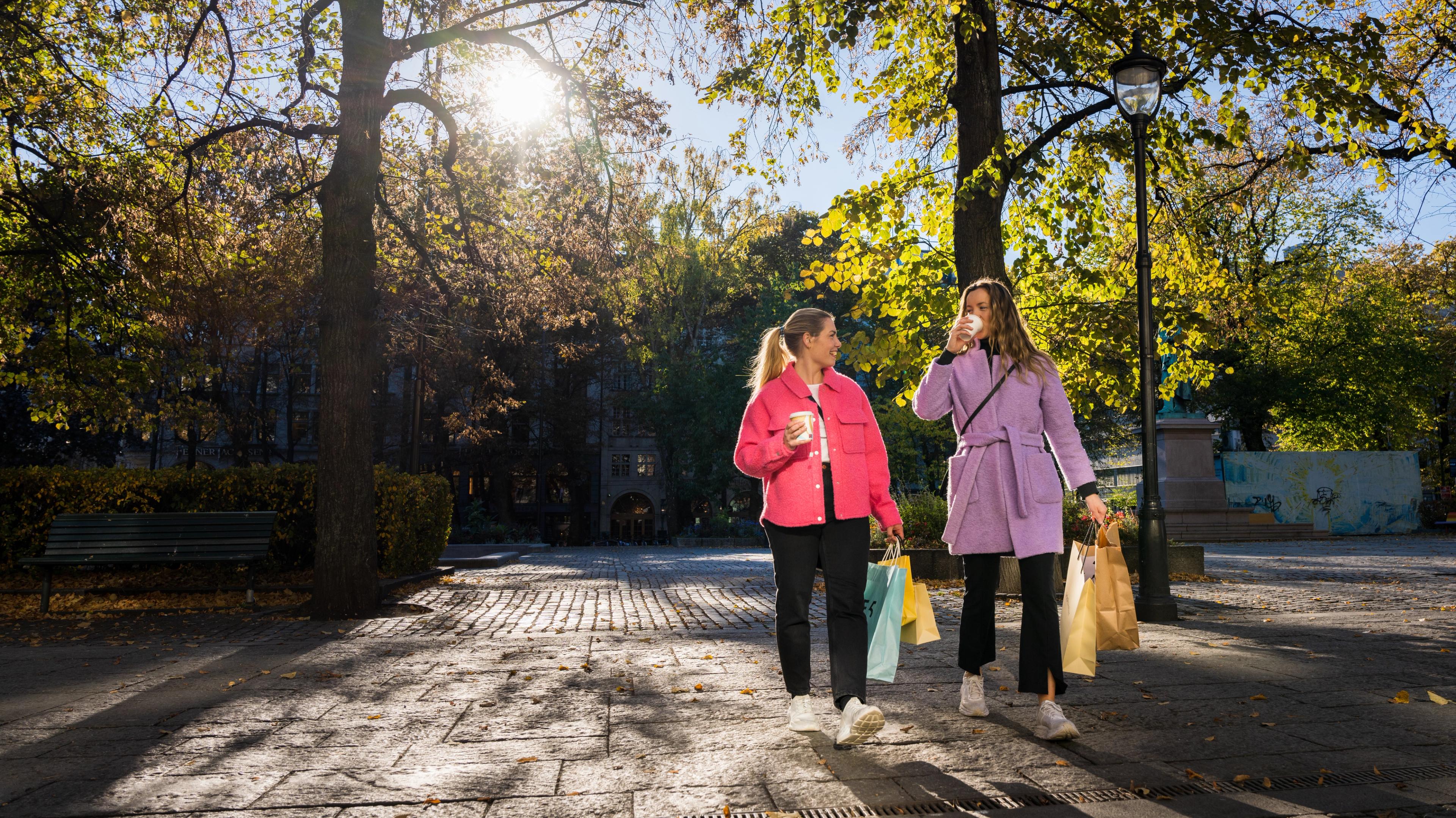Two girls are laughing and drinking a coffee on the go in the shopping street Karl Johan in Oslo