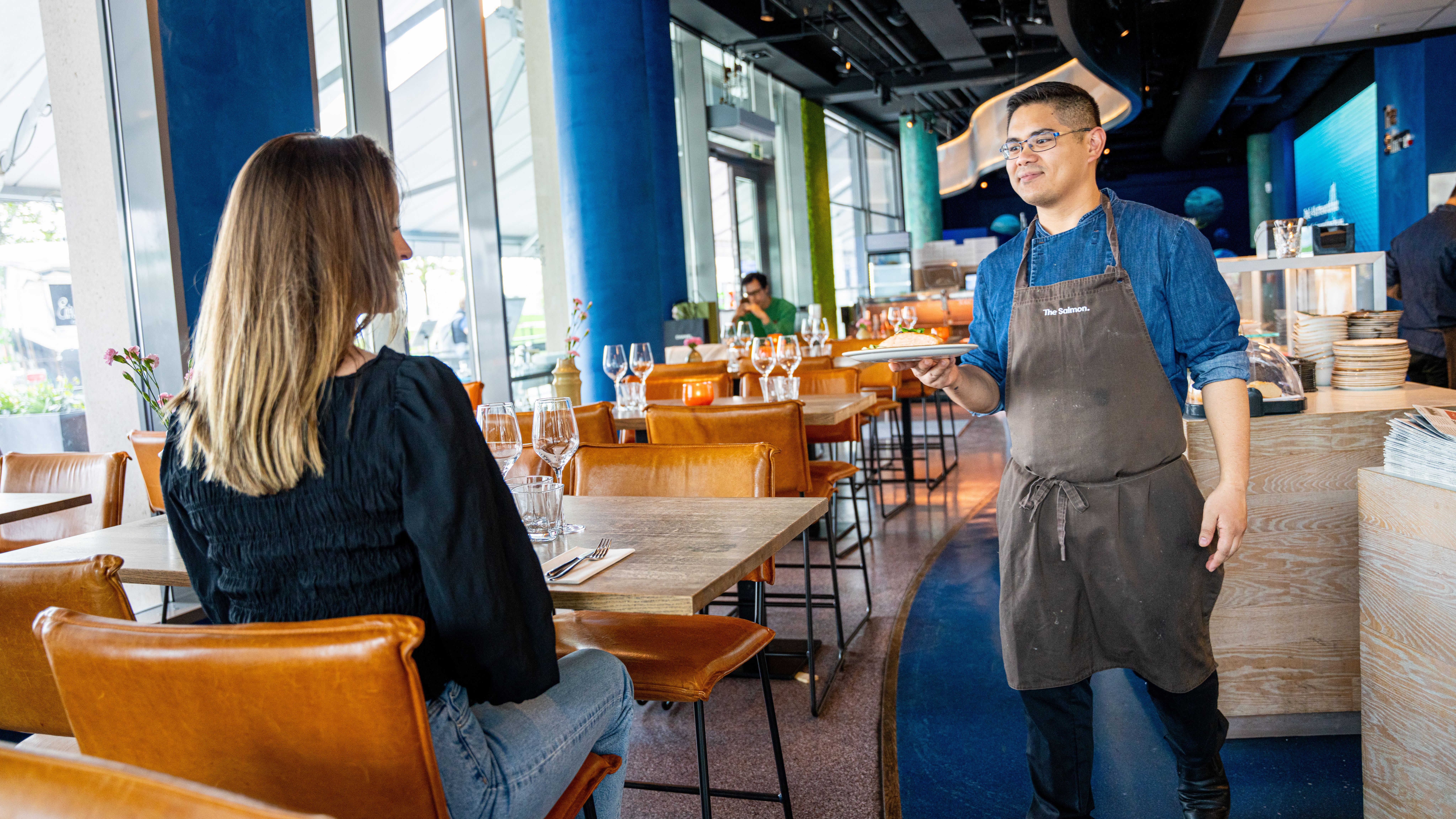 Chef serving grilled salmon to a woman at The Salmon restaurant in Oslo