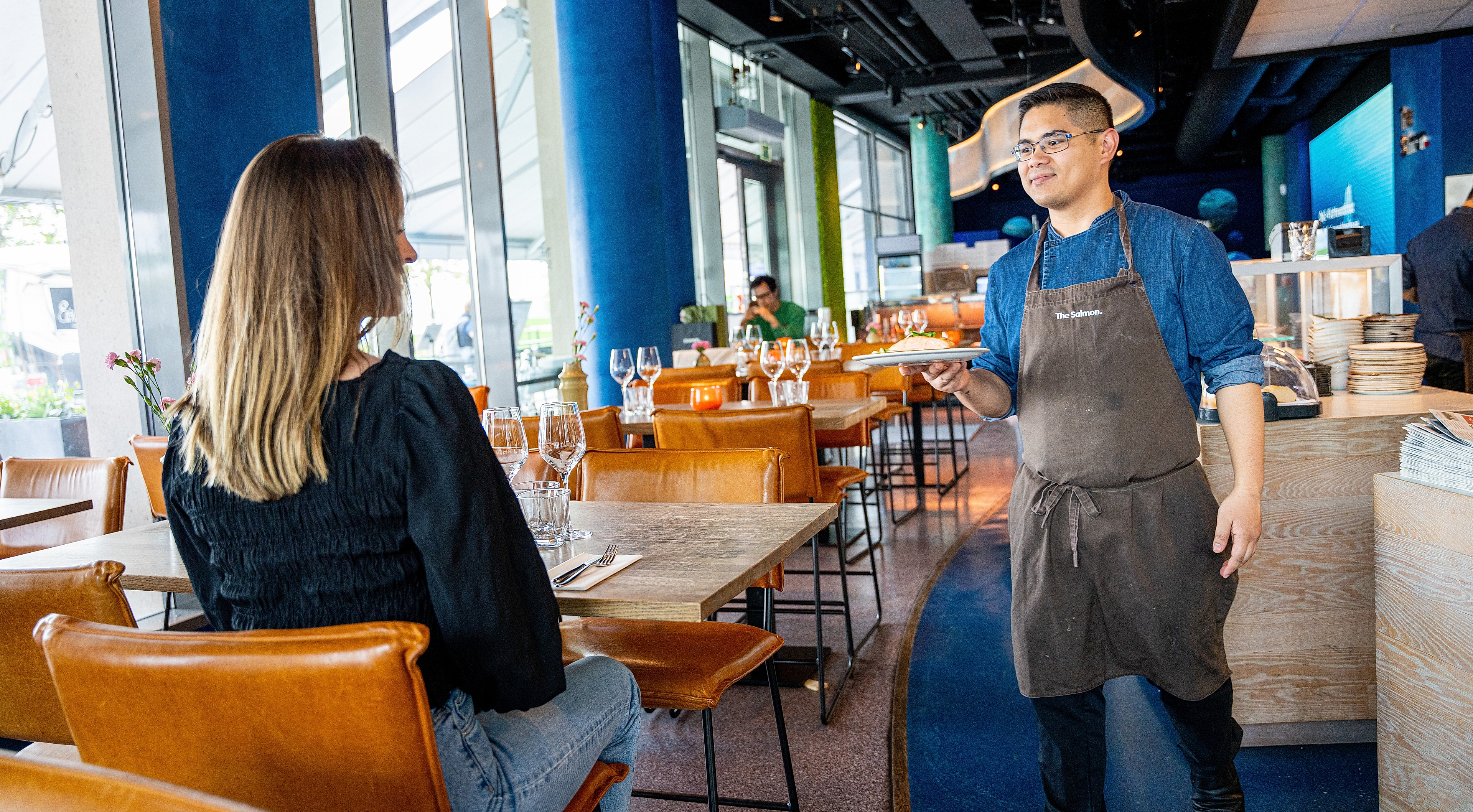 Chef serving grilled salmon to a woman at The Salmon restaurant in Oslo