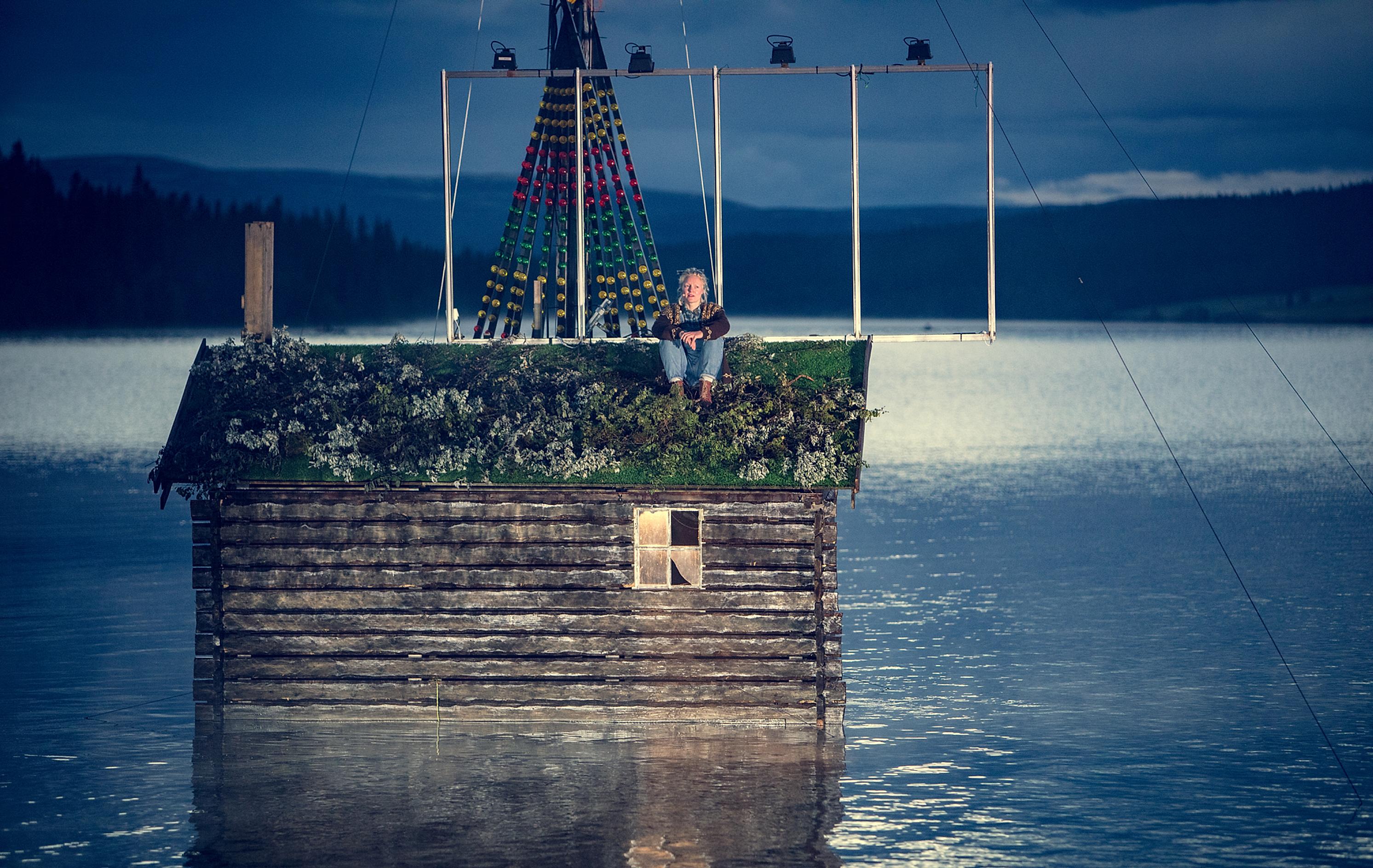 An actor sitting on the roof of a cabin in the water, Peer Gynt Festival, Gålå, Eastern Norway
