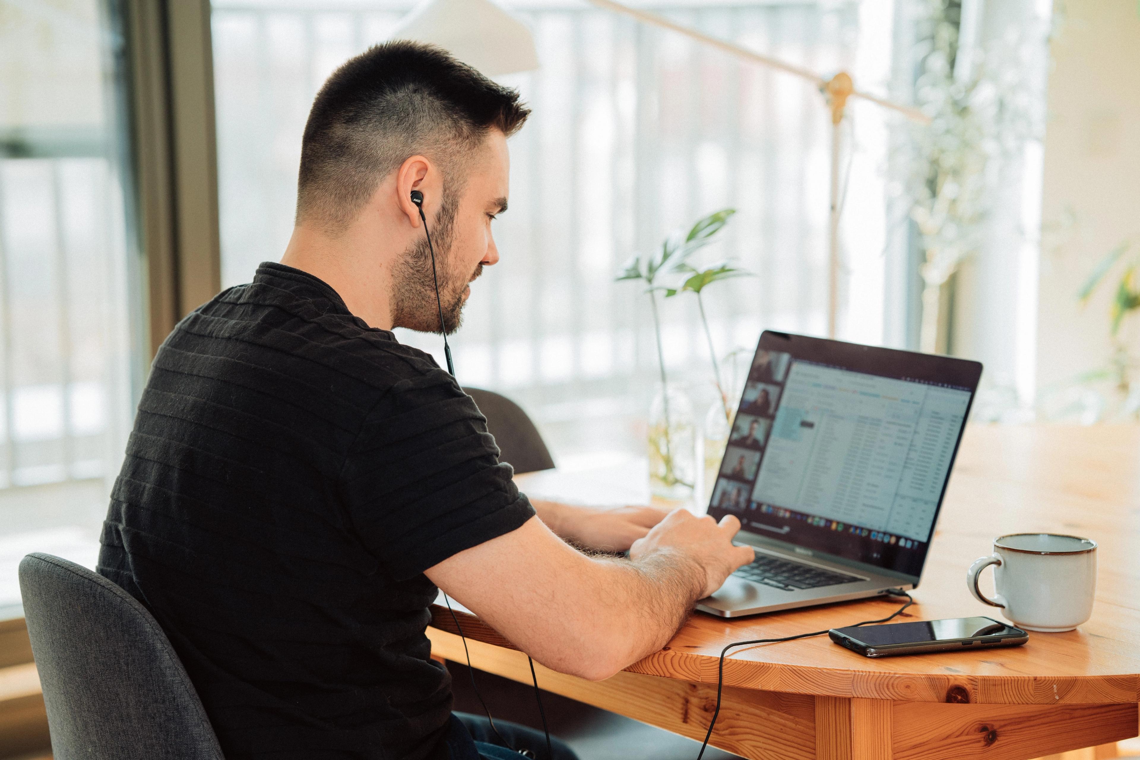 A young man in a black T-shirt in a conference meeting on his laptop
