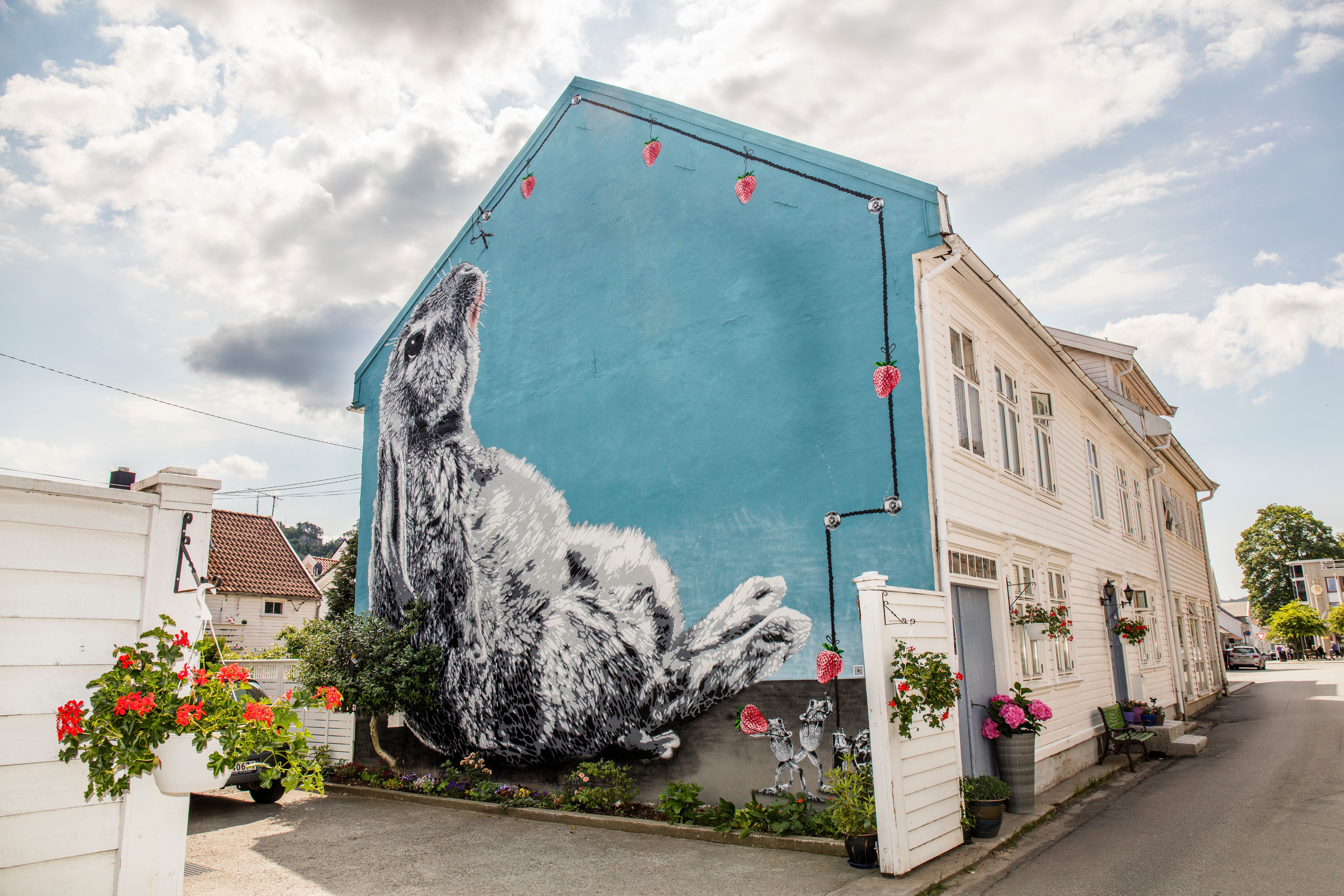Gatukonst som täcker hela gaveln av ett vitt trähus i Flekkefjord i regionen Sørlandet (södra Norge). Motivet är en kanin med blå bakgrund