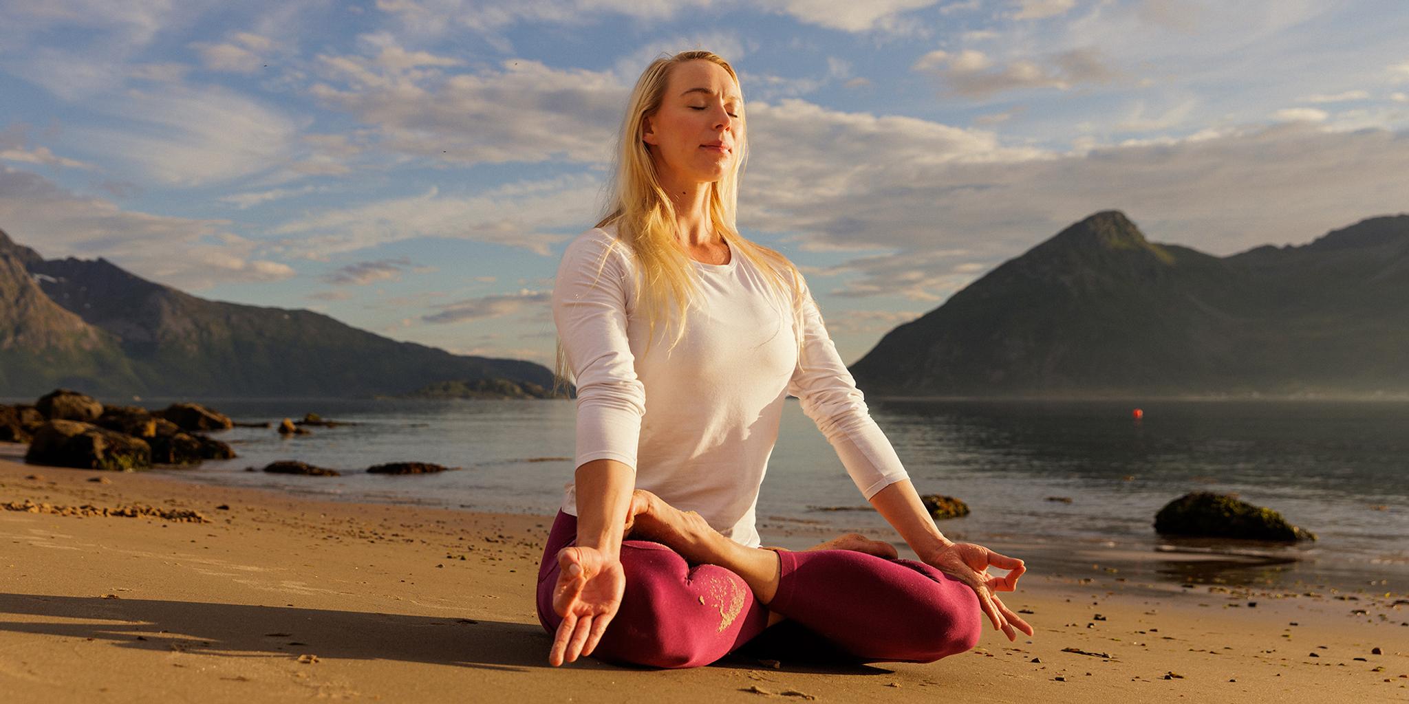 A woman sitting in lotus yoga position on the beach in the midnight sun, Northern Norway.