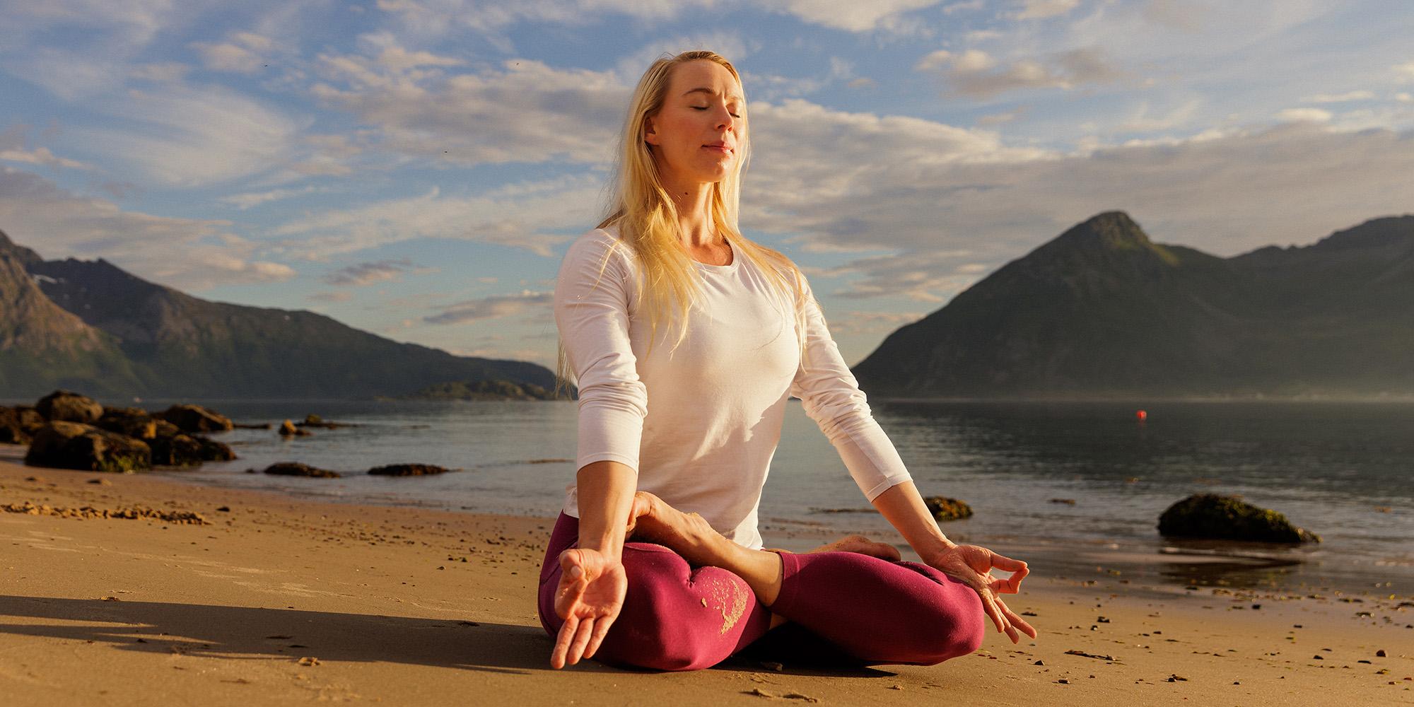 A woman sitting in lotus yoga position on the beach in the midnight sun, Northern Norway.