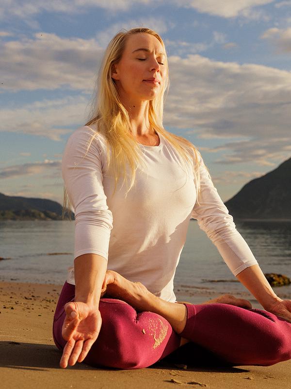 A woman sitting in lotus yoga position on the beach in the midnight sun, Northern Norway.