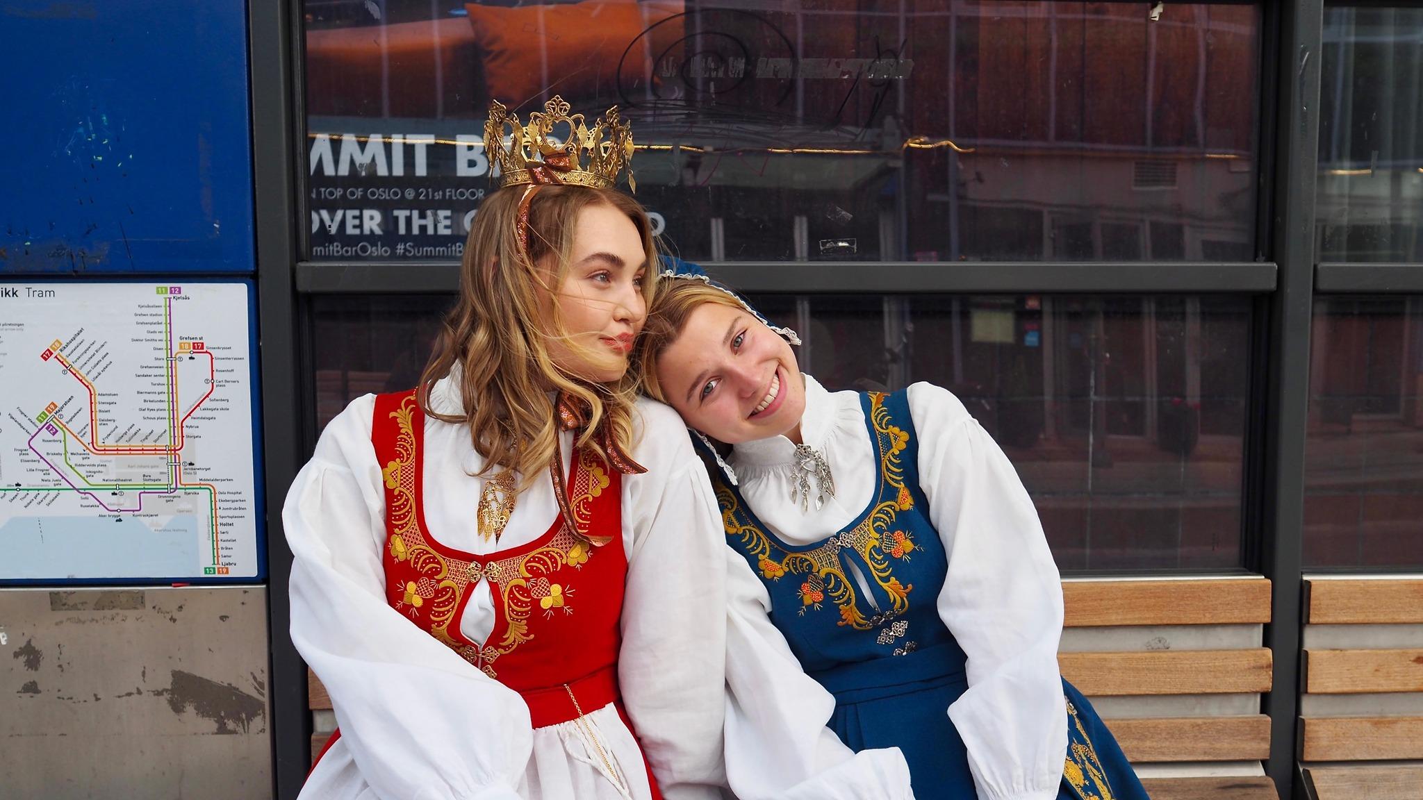 Two women waiting for the bus wearing traditional costumes, "Romeriksbunaden", in Eastern Norway