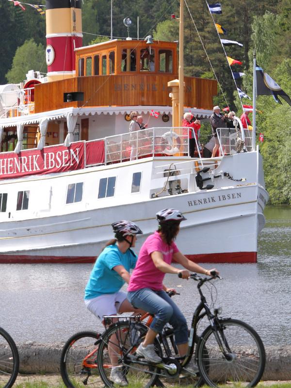 Fietsers rijden voorbij een boot op het Telemarkkanaal over de Nationale fietsroute in Oost-Noorwegen