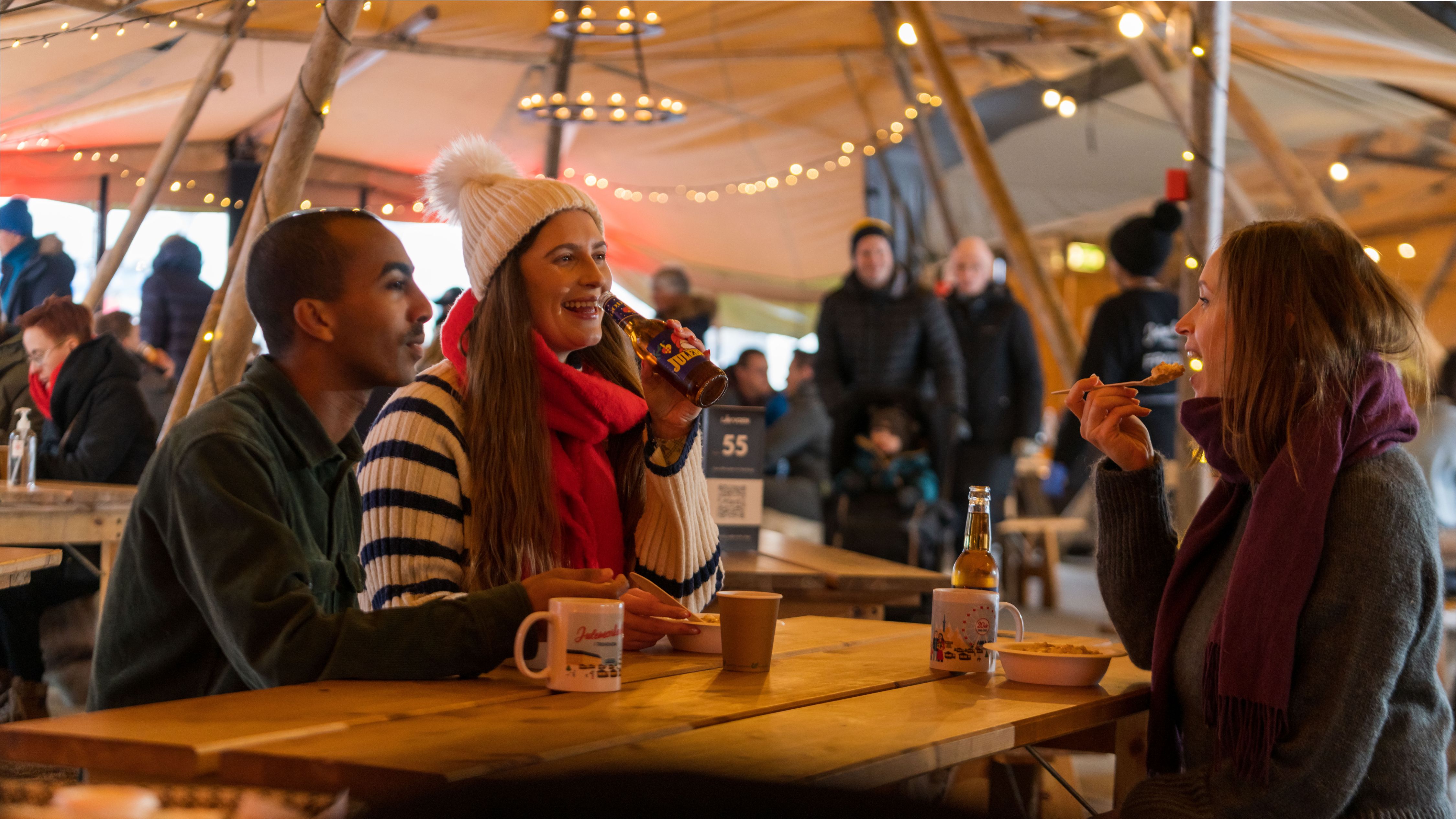 Three people enjoying a meal in the lavvo at the Christmas market in Trondheim, Trøndelag, Norge.