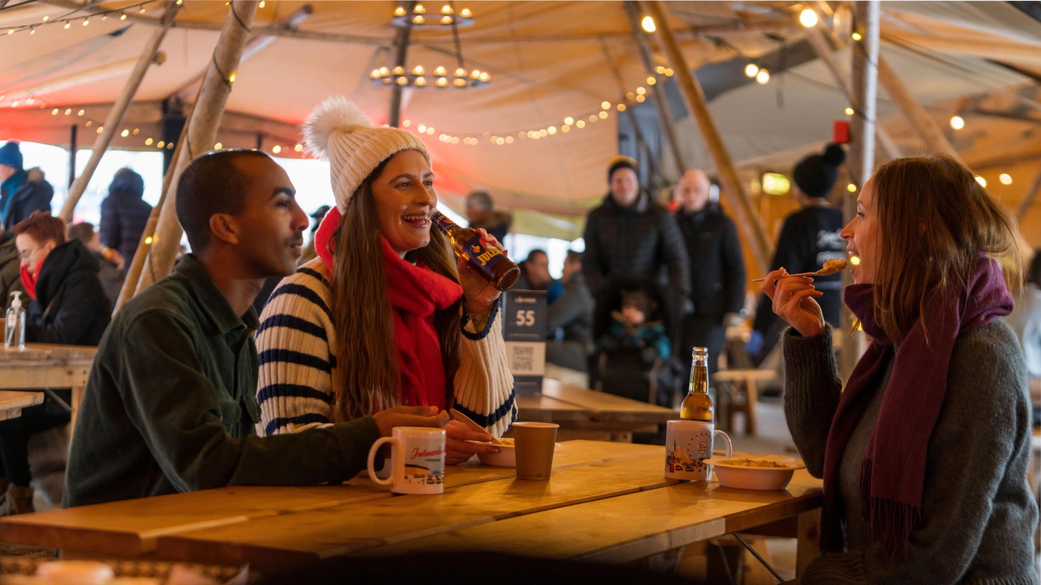 Three people enjoying a meal in the lavvo at the Christmas market in Trondheim, Trøndelag, Norge.