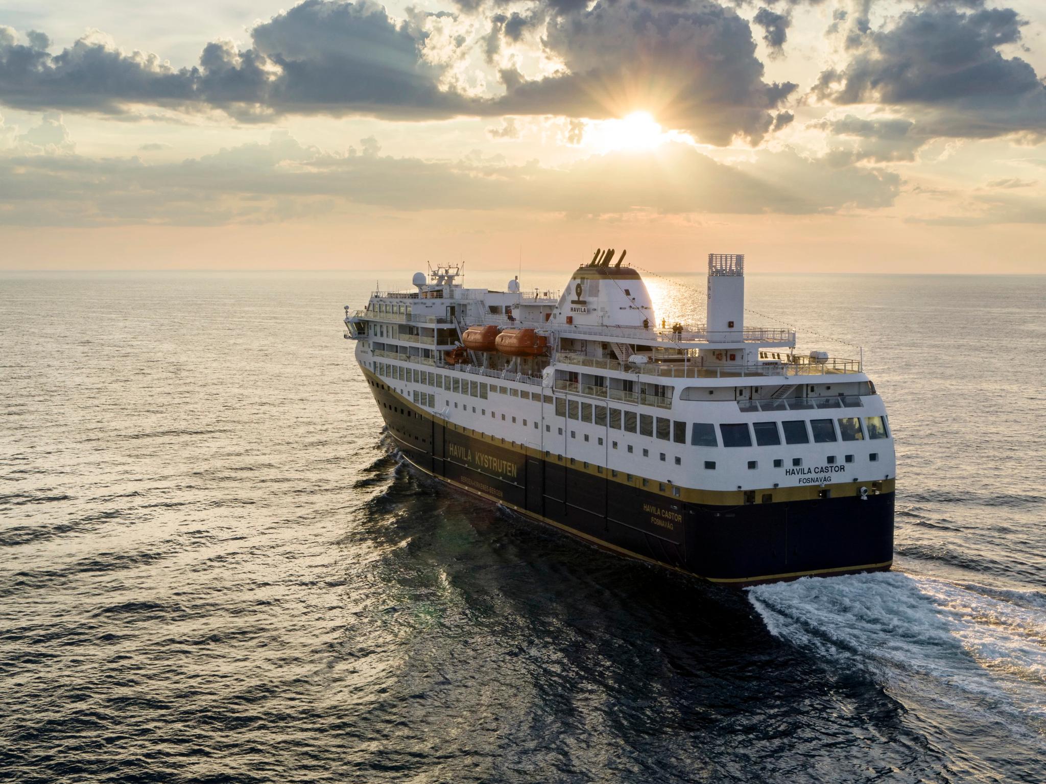 A Havila ship sailing across calm ocean waters at sunset.