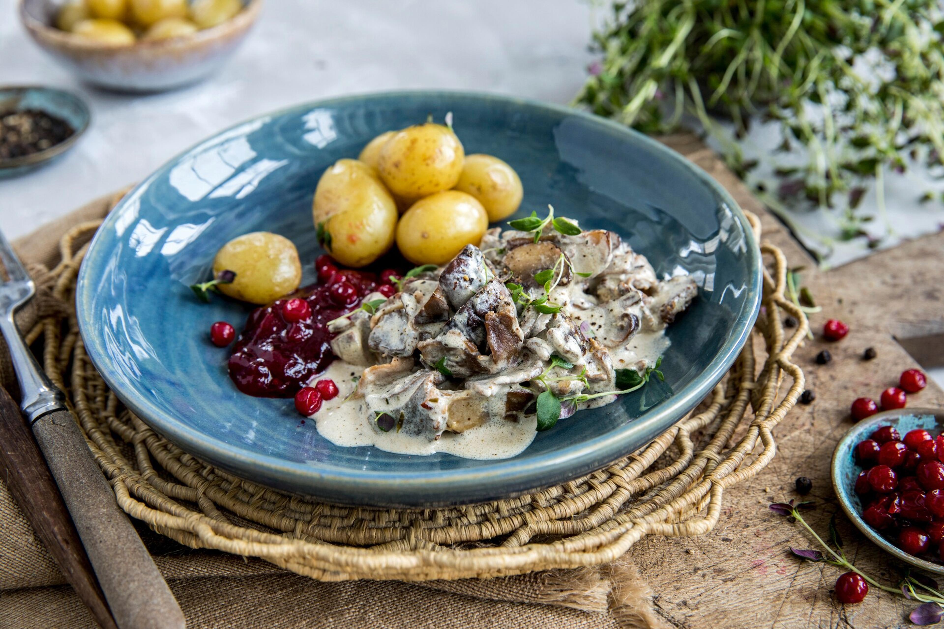 Venison stew on a plate, with potatoes and lingonberries.