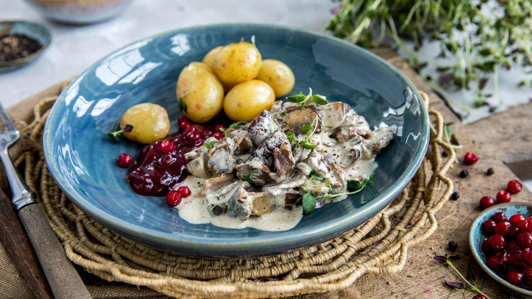 Venison stew on a plate, with potatoes and lingonberries.