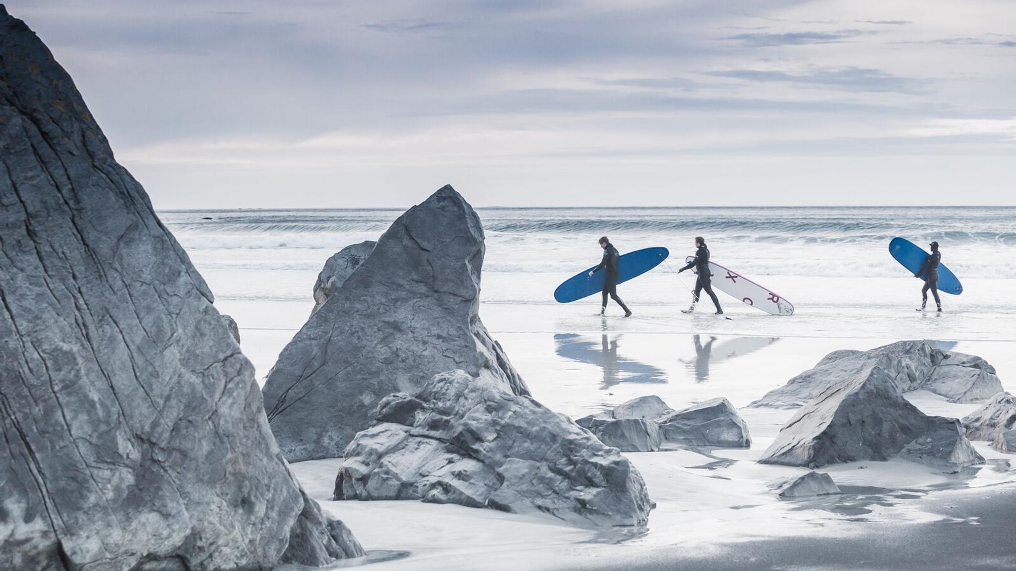 Three people surfing at Flakstad in Lofoten in wintertime