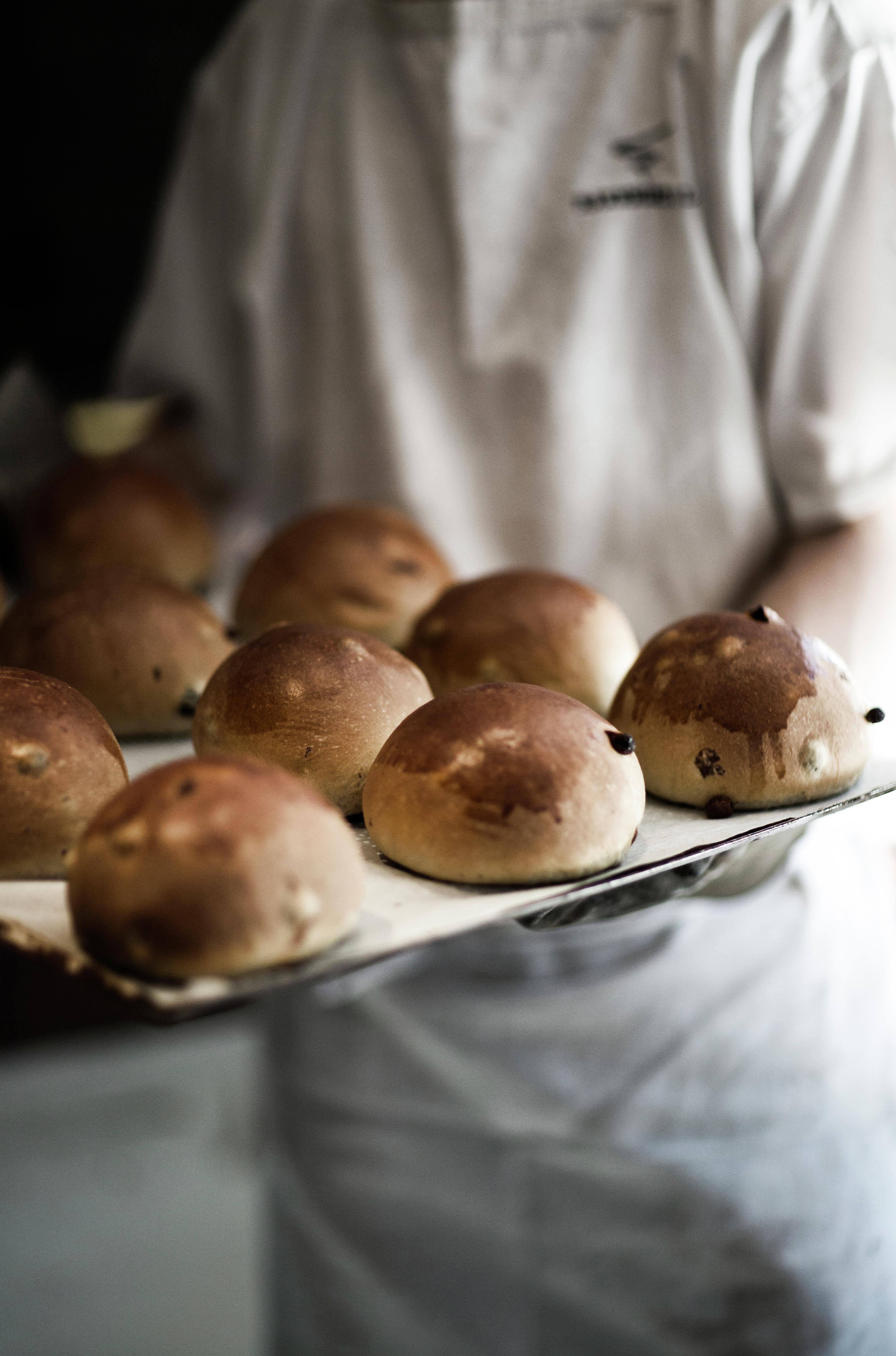Fresh sweet buns on a tray held by a baker