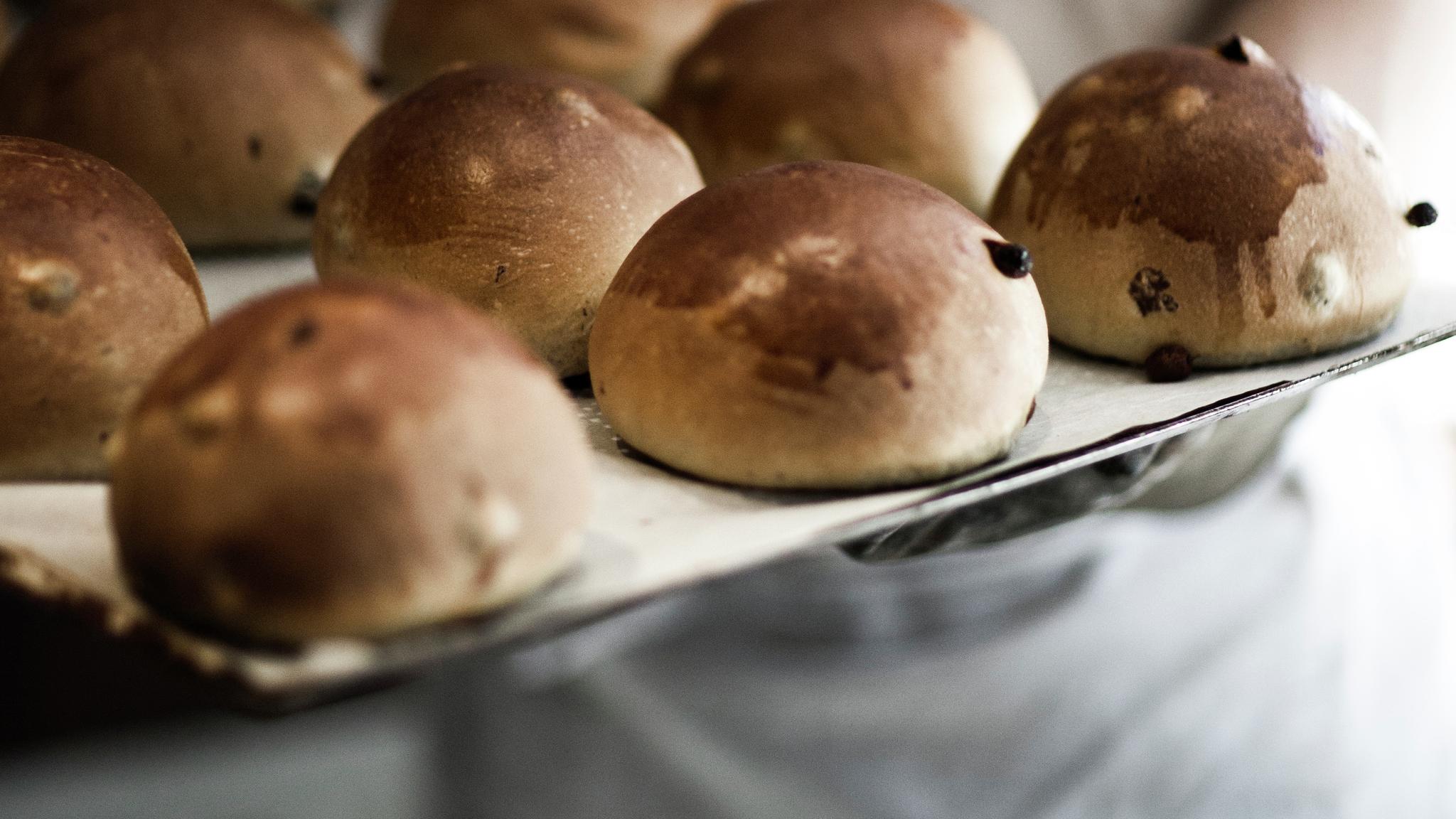 Fresh sweet buns on a tray held by a baker