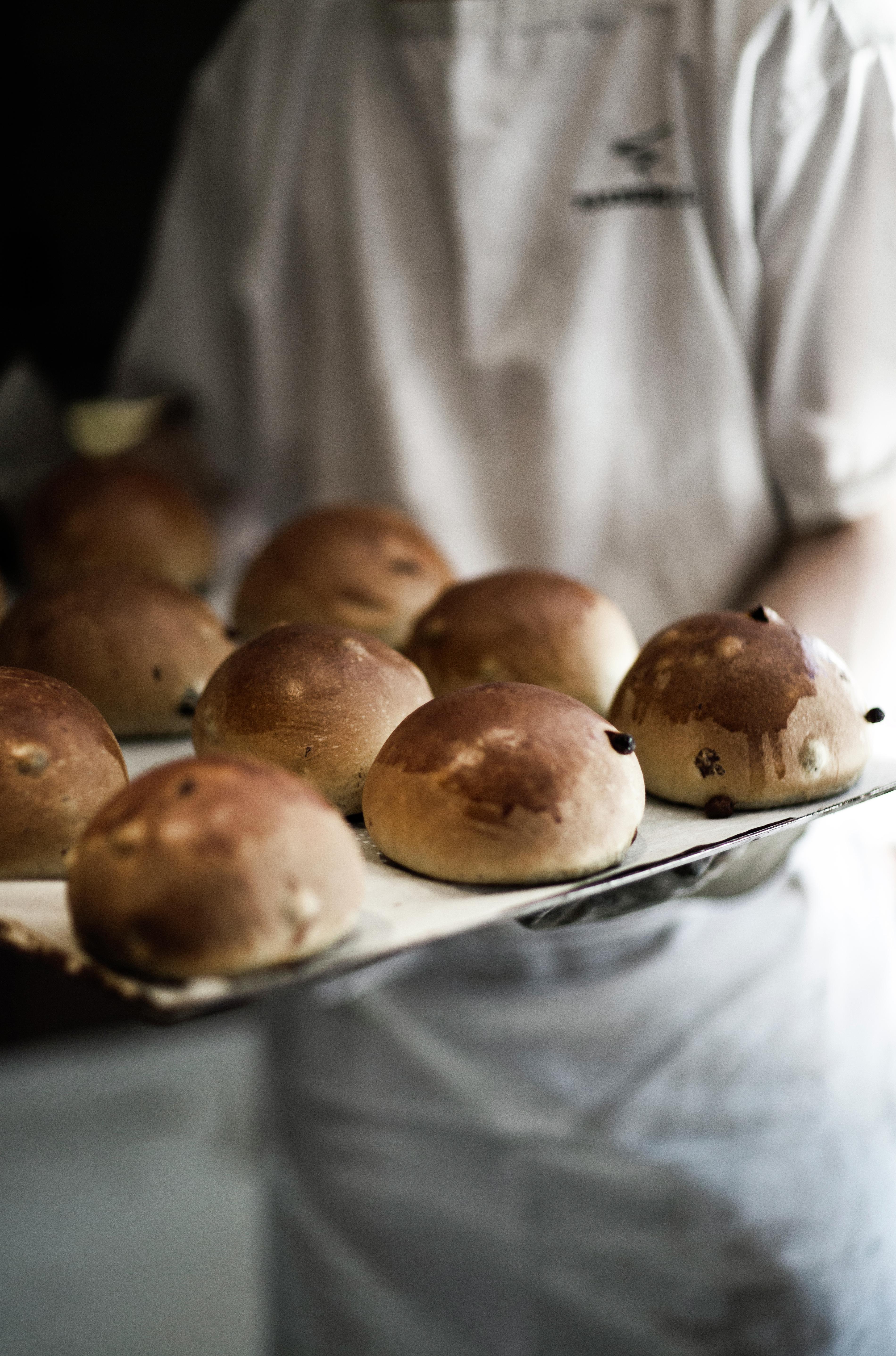Fresh sweet buns on a tray held by a baker