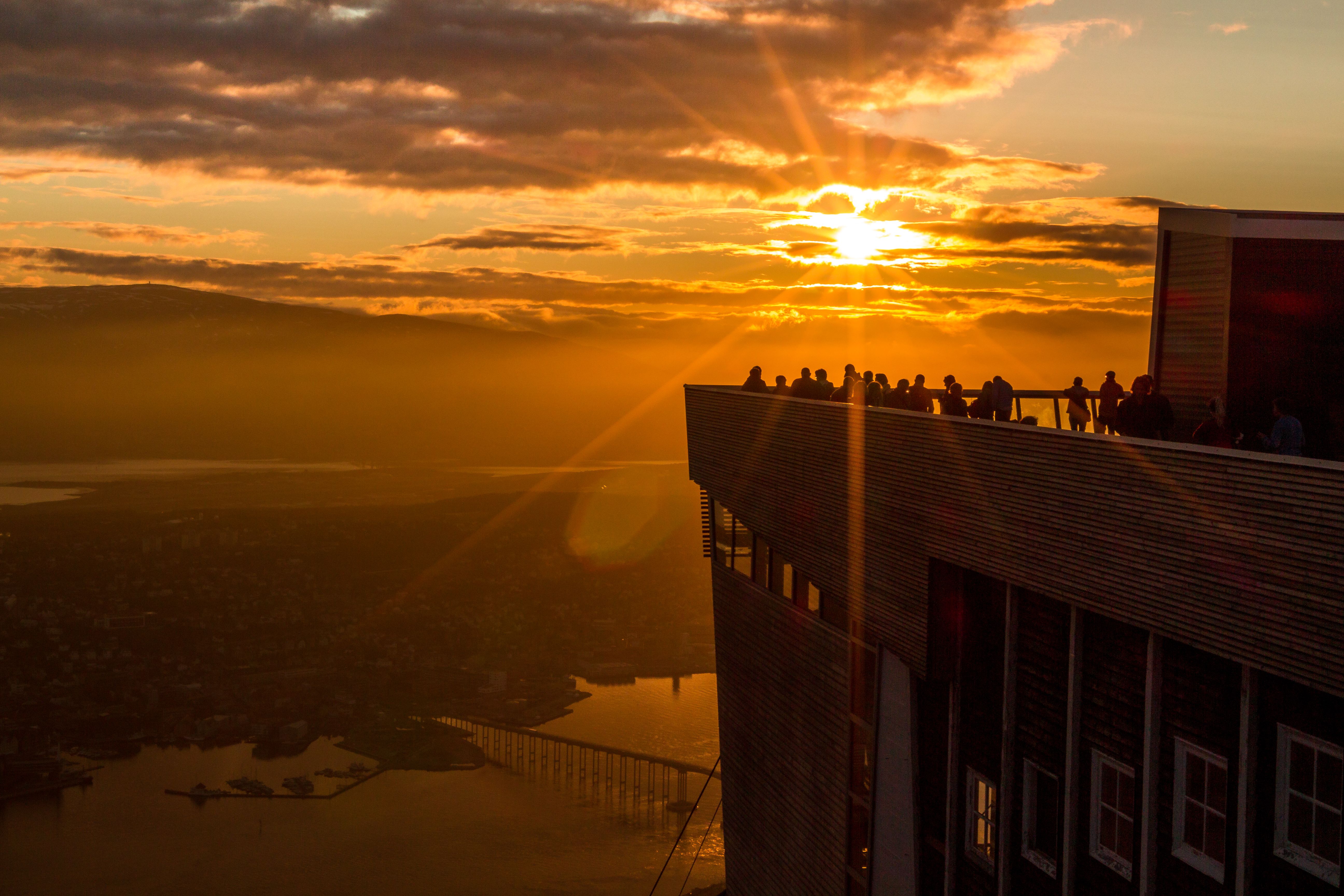 People are standing at the rooftop of the cable car in Tromsø, Northern Norway, admiring the midnight sun.