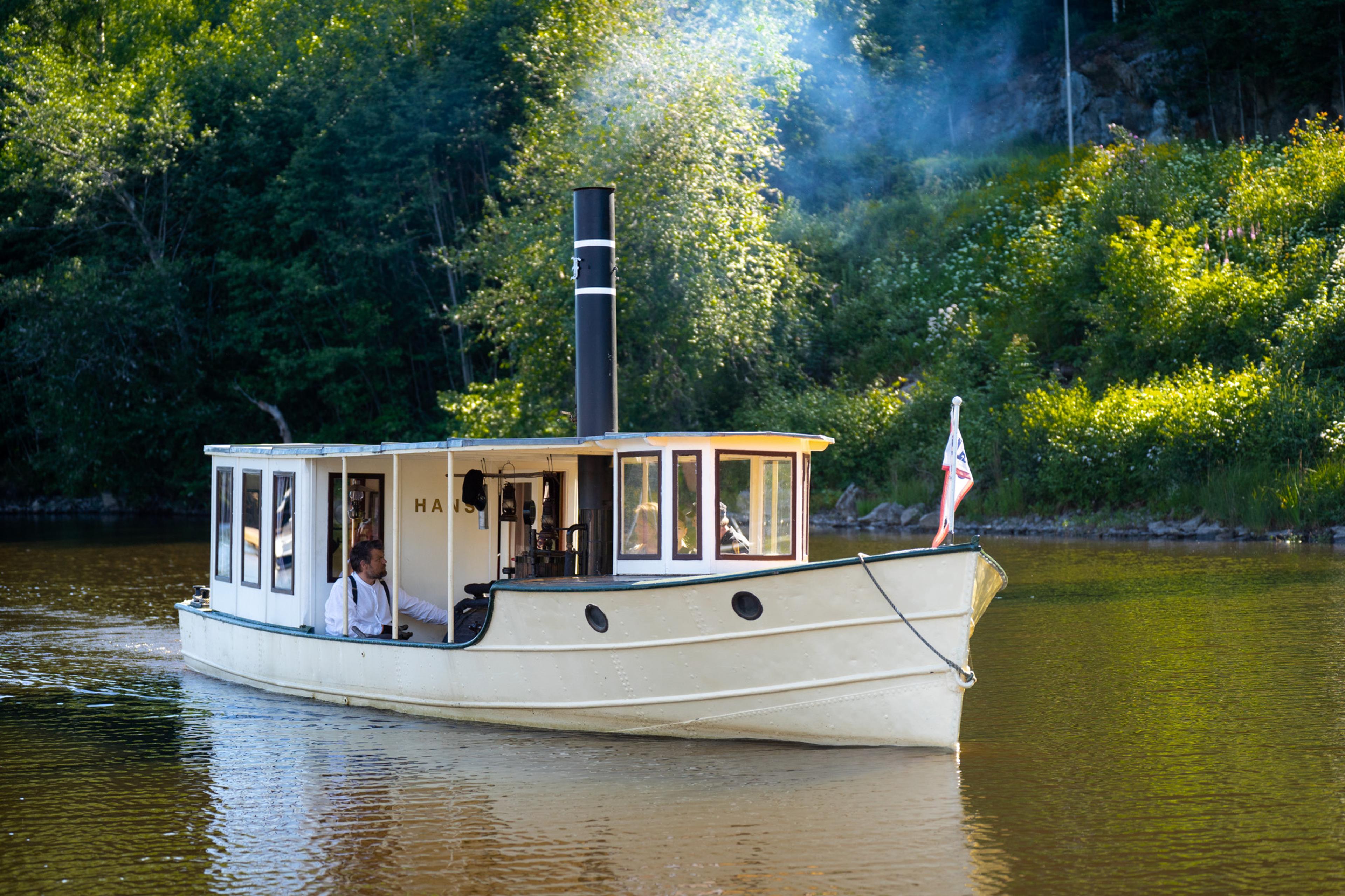 A small steamship surrounded by lush green scenery