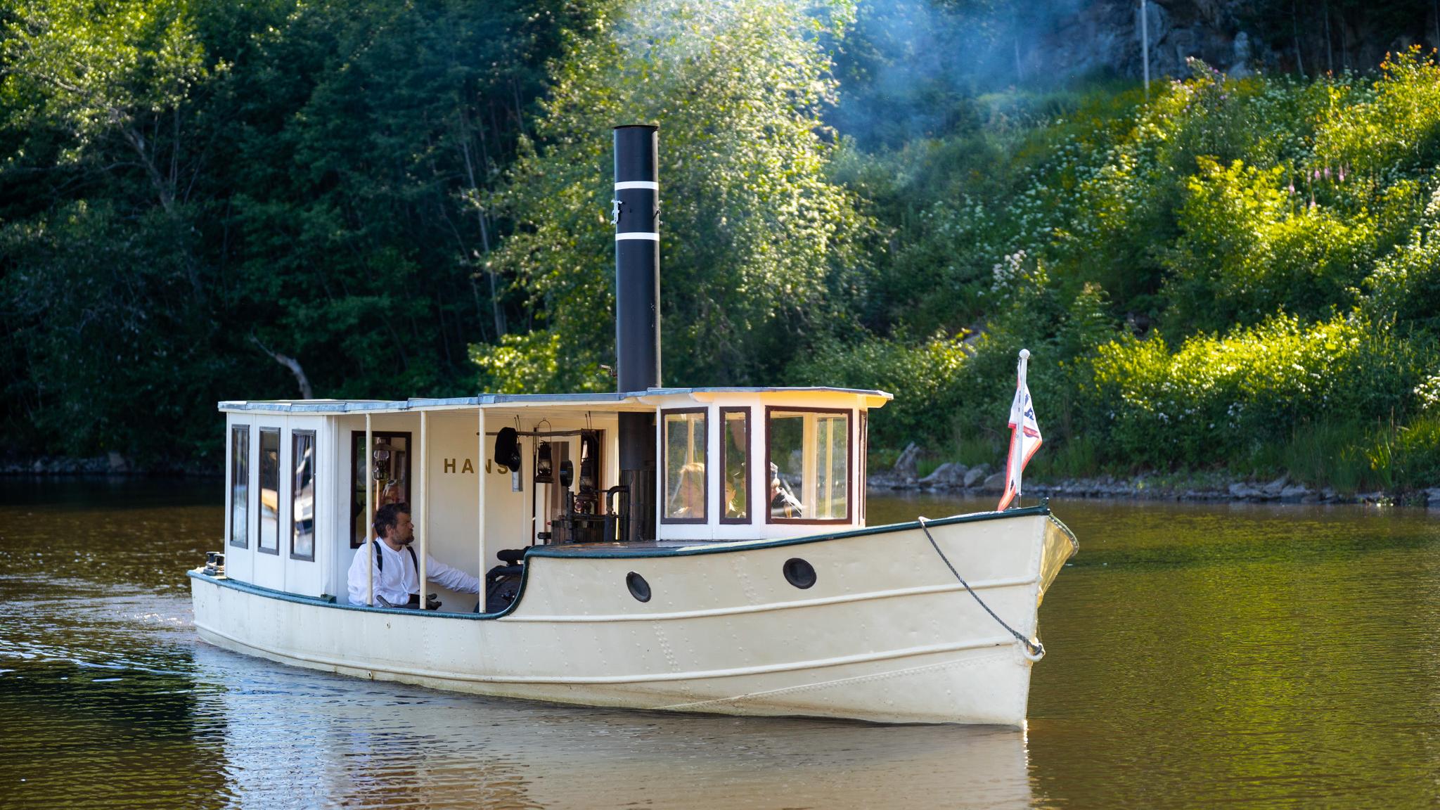 A small steamship surrounded by lush green scenery