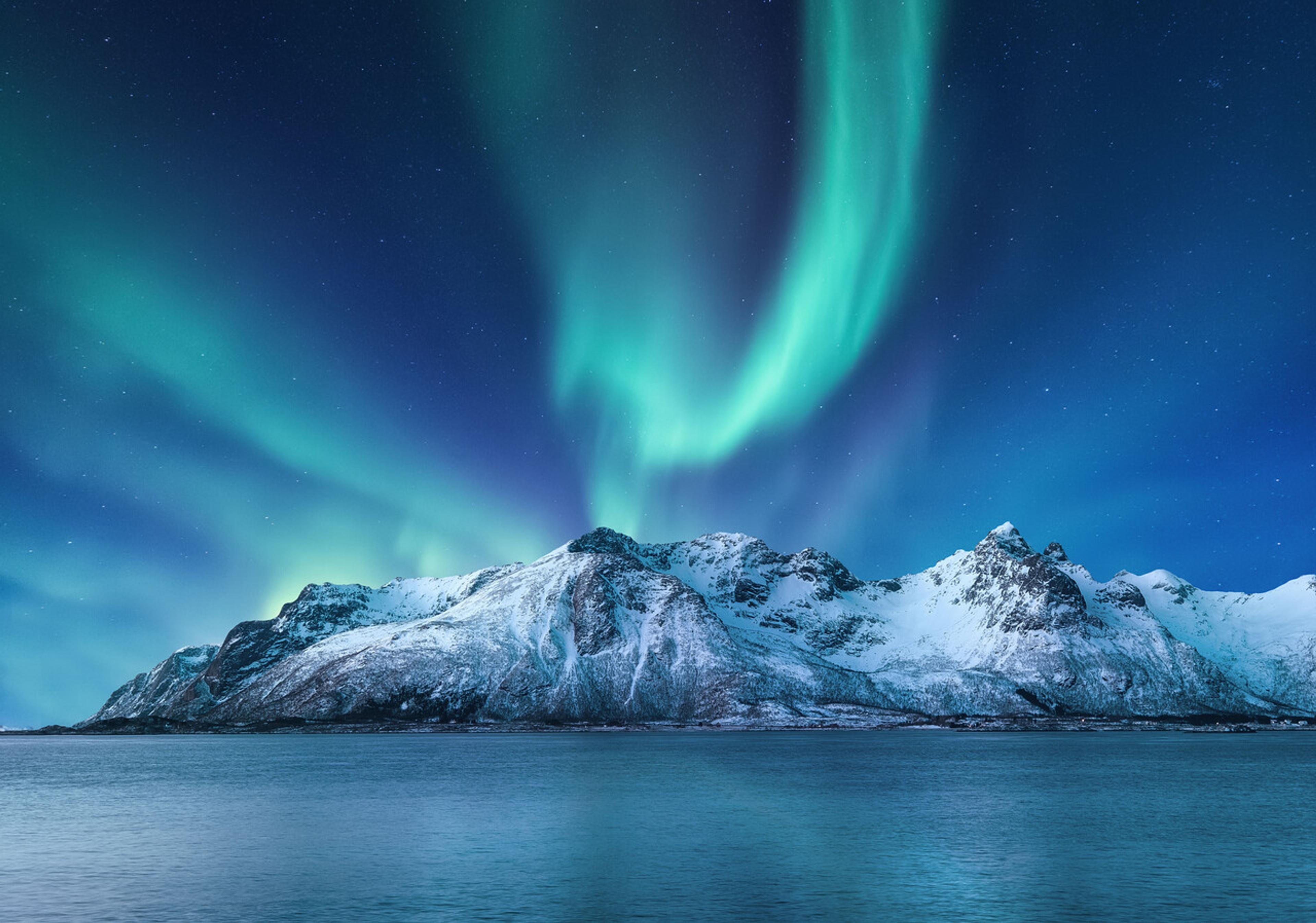 Northern lights over snow-capped mountains and ocean surface