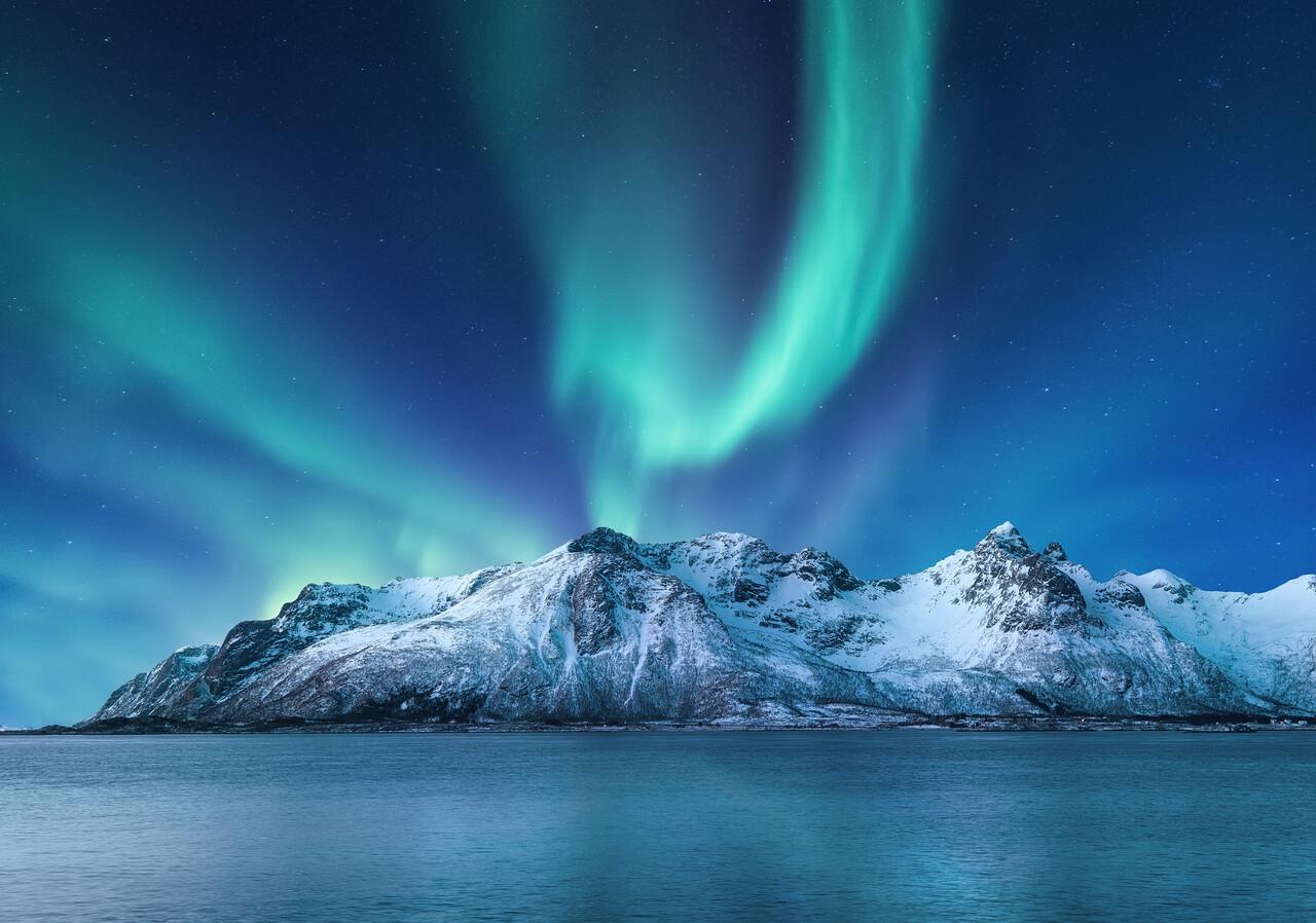 Northern lights over snow-capped mountains and ocean surface