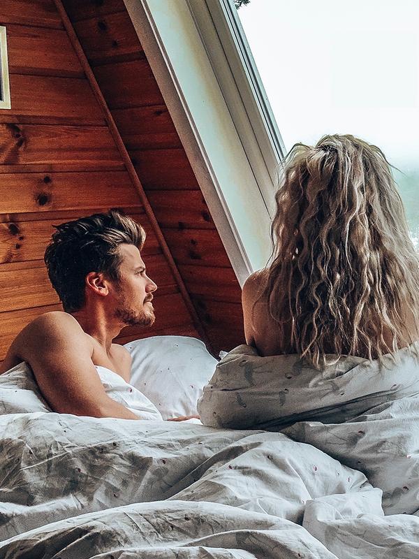 En dame og en mann sitter i sengen og ser ut av vinduet på Mikrohyttene i Kragerø i Telemark, Østlandet