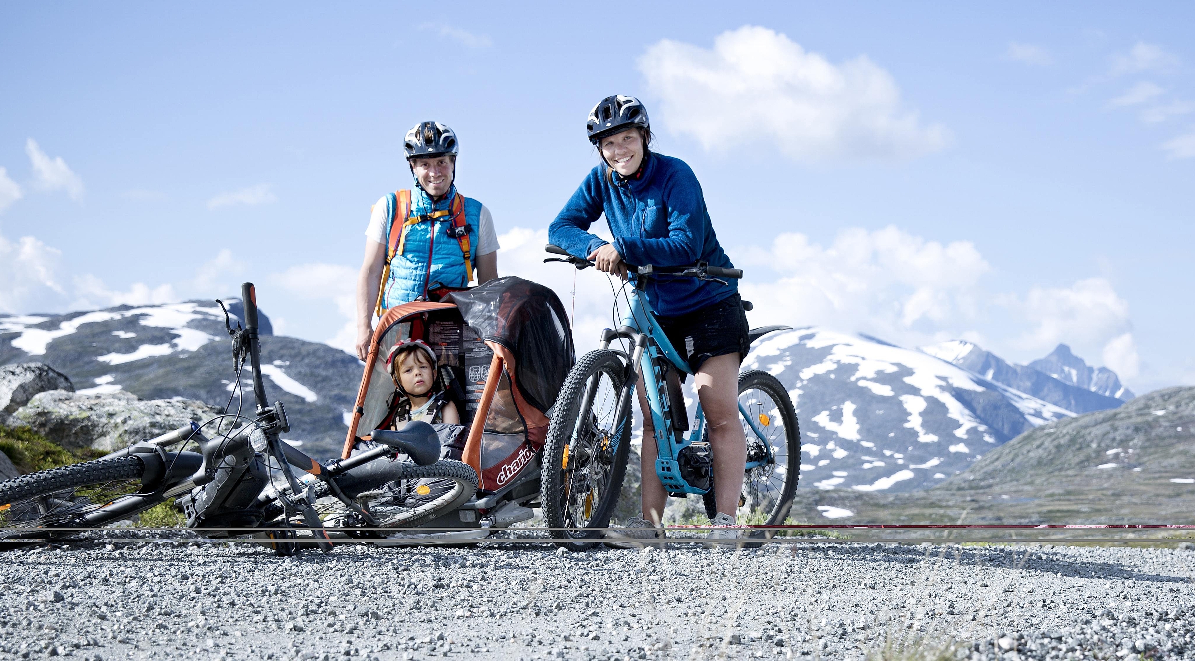 A family of three with e-bikes on a road near Åndalsnes, Fjord Norway