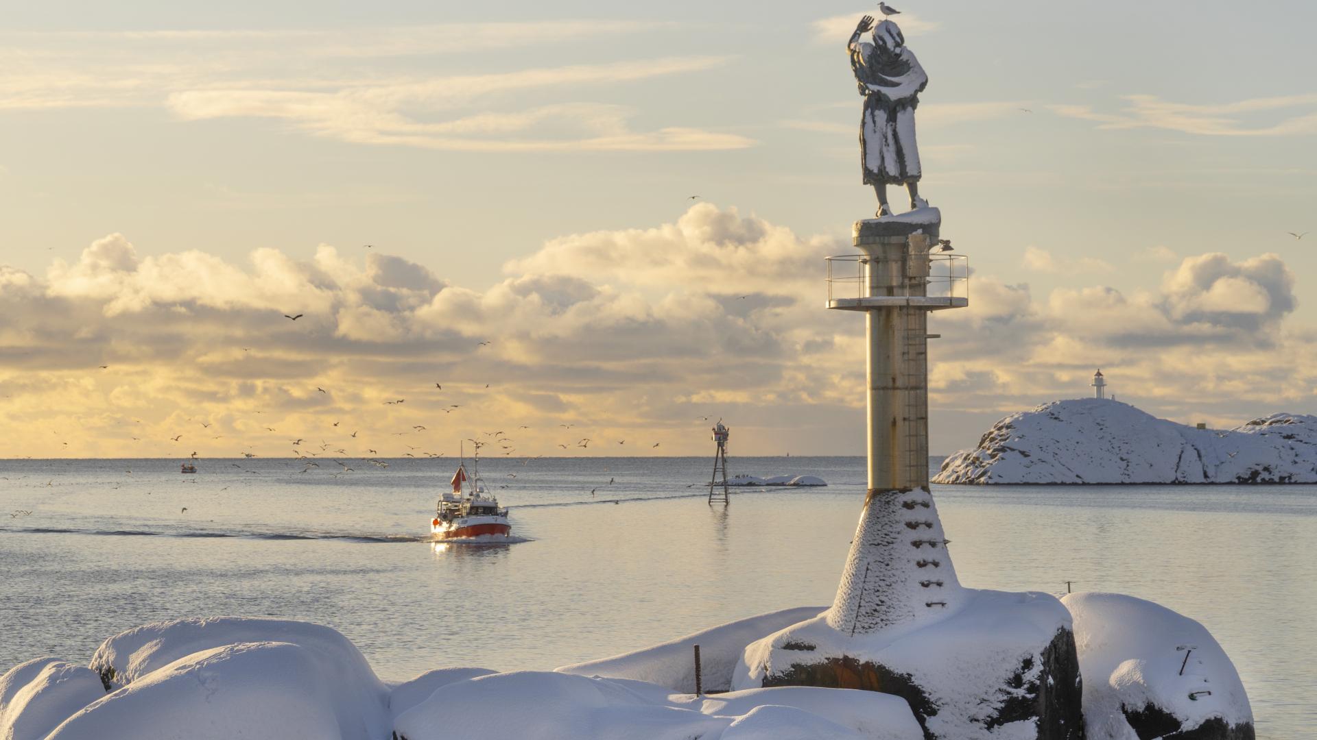 Skrei fishing boat by Fiskarkona statue in Lofoten