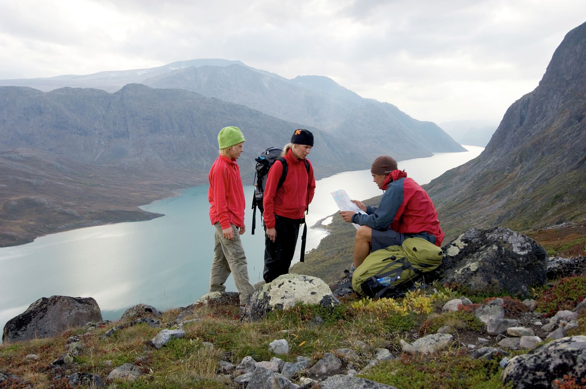 Two adults and a child are studying the map and compass on a mountain hike