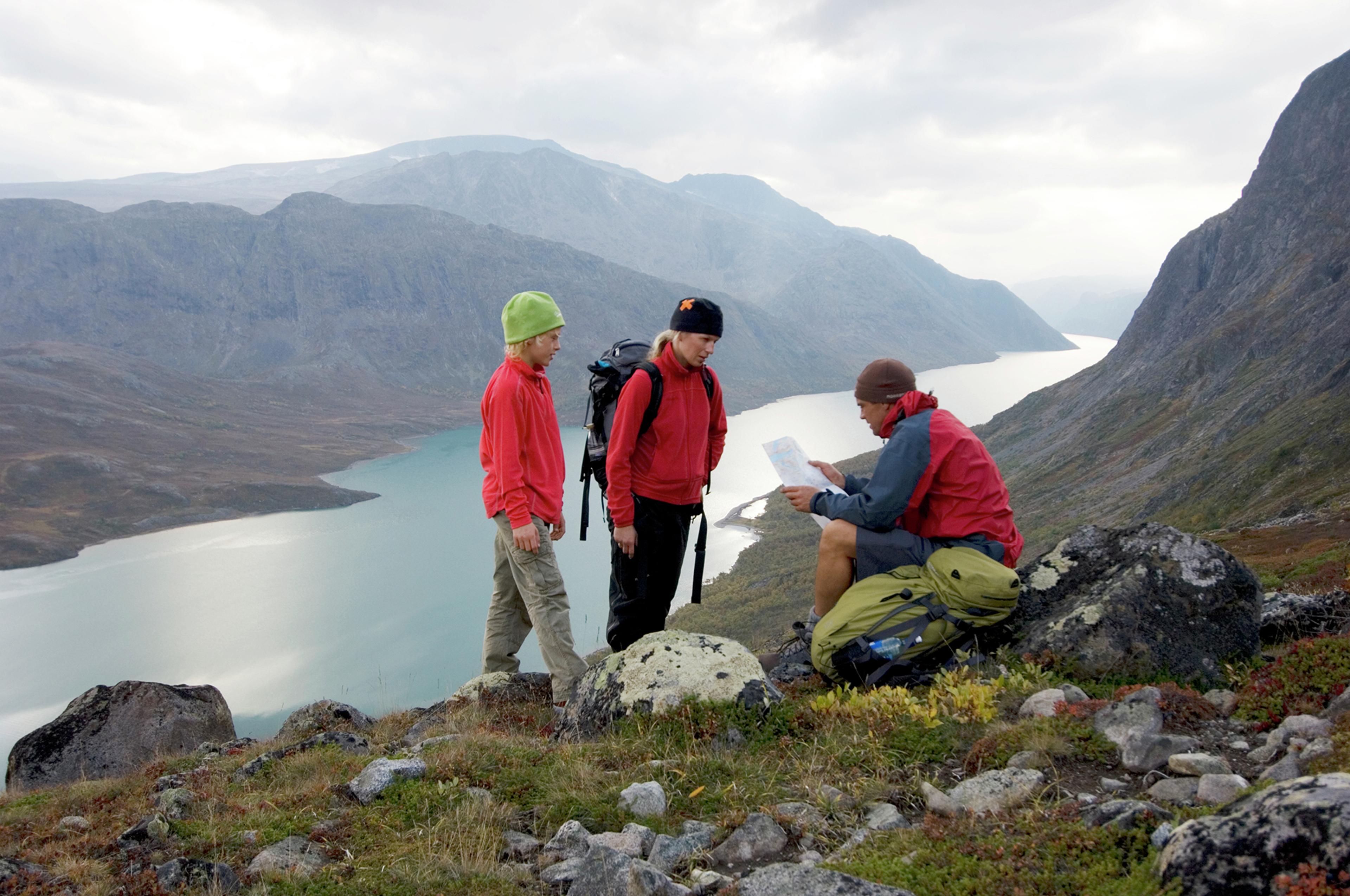 Two adults and a child are studying the map and compass on a mountain hike