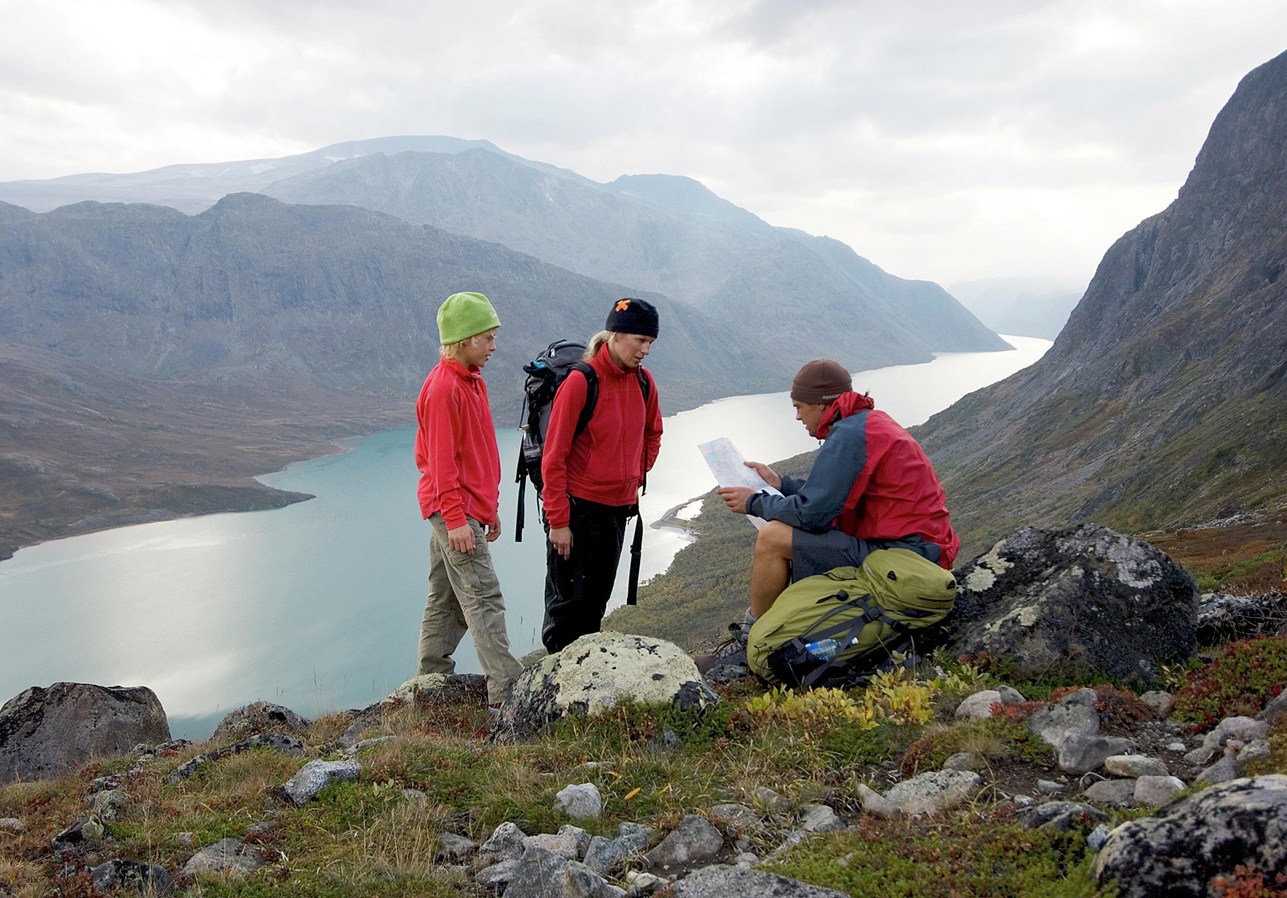 Two adults and a child are studying the map and compass on a mountain hike