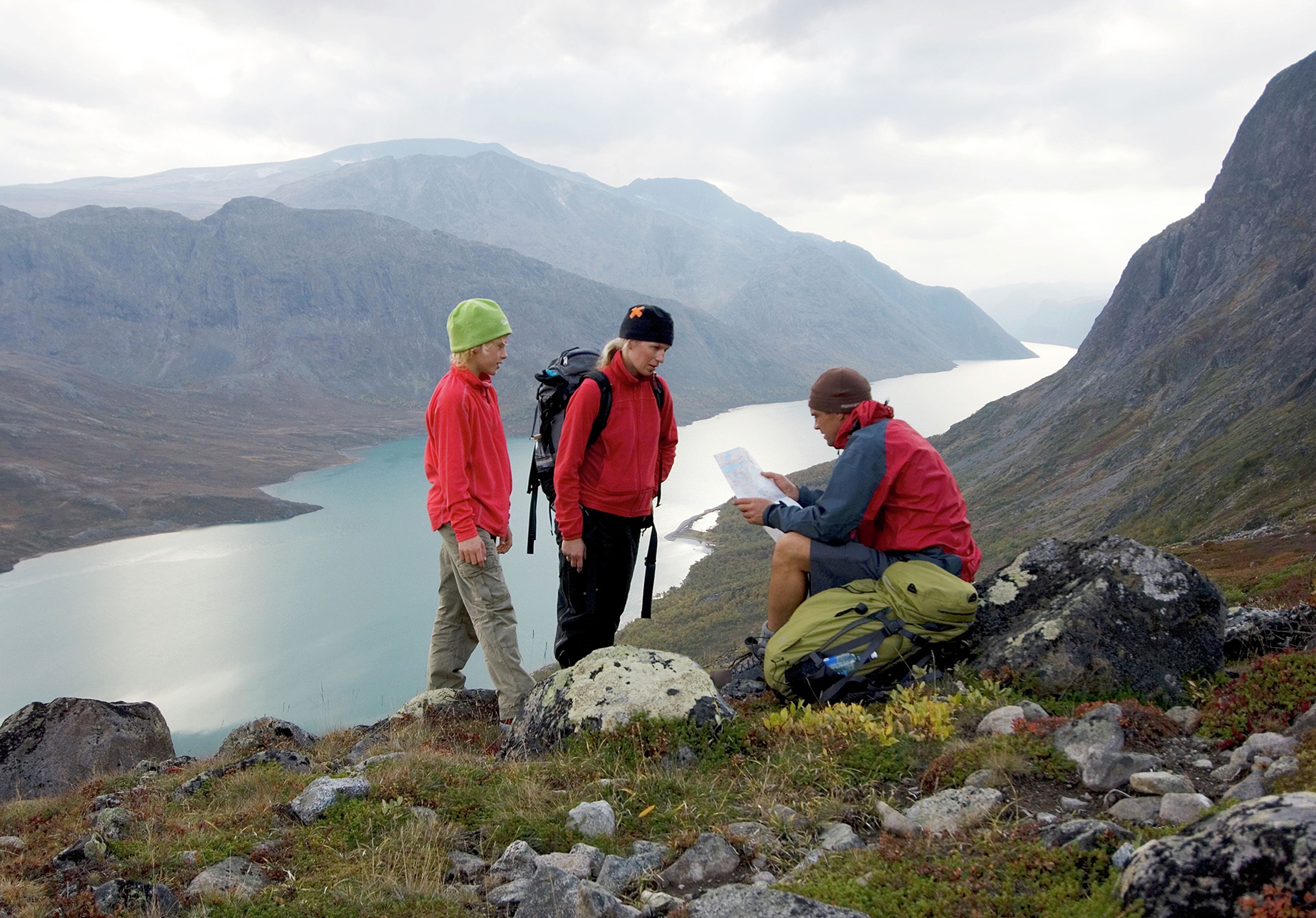 Two adults and a child are studying the map and compass on a mountain hike