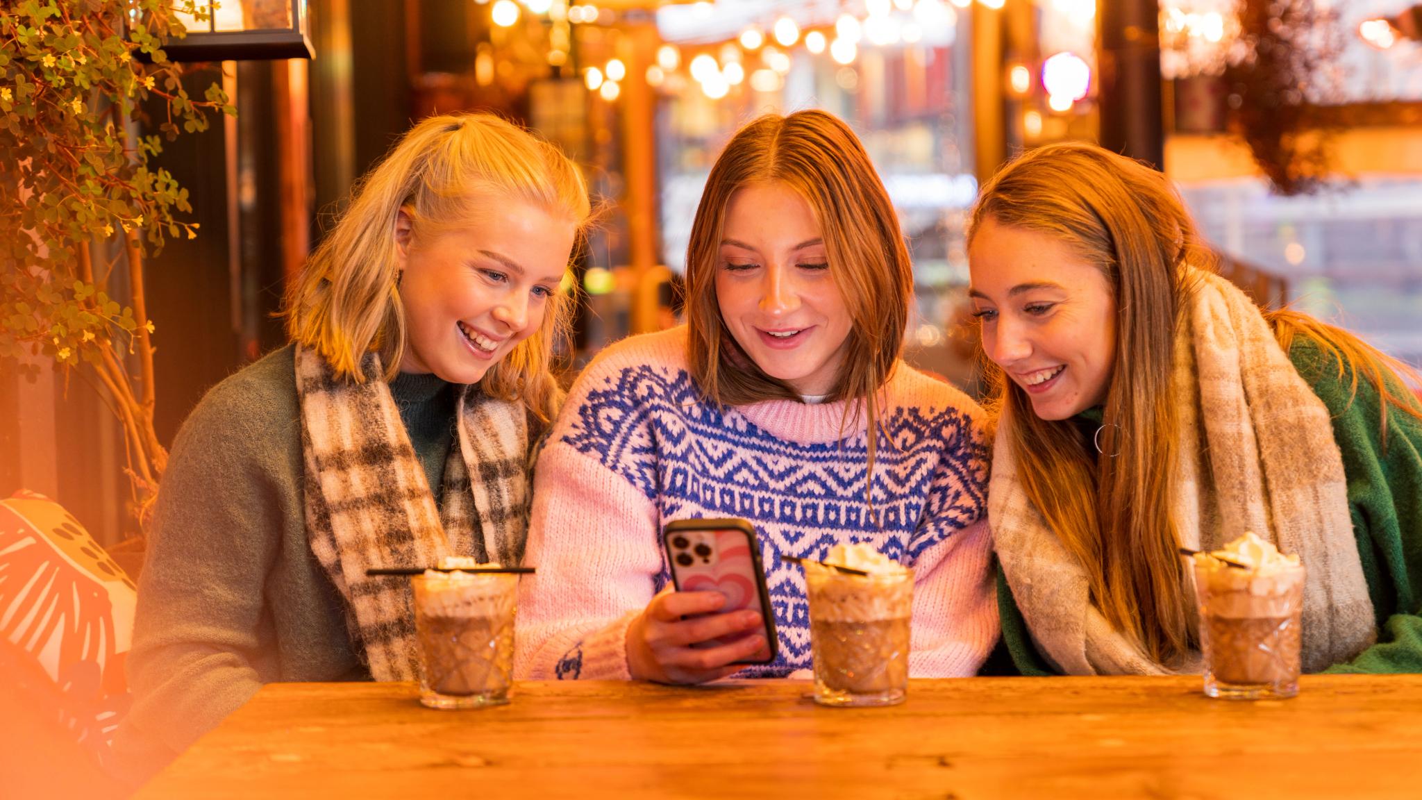 Girls drinking hot chocolate at café in Oslo looking at the phone