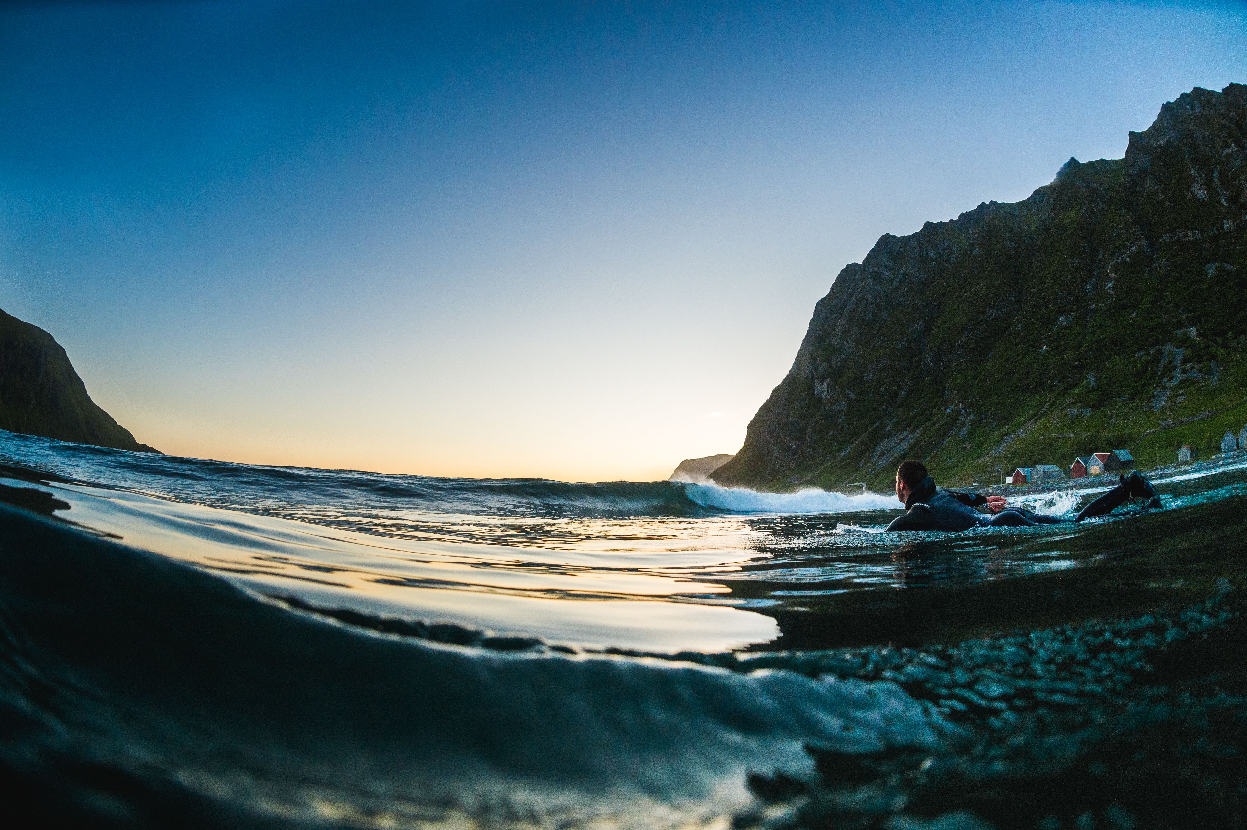 A man on lying on a surfboard swims towards the open sea at Hoddevik in Fjord Norway