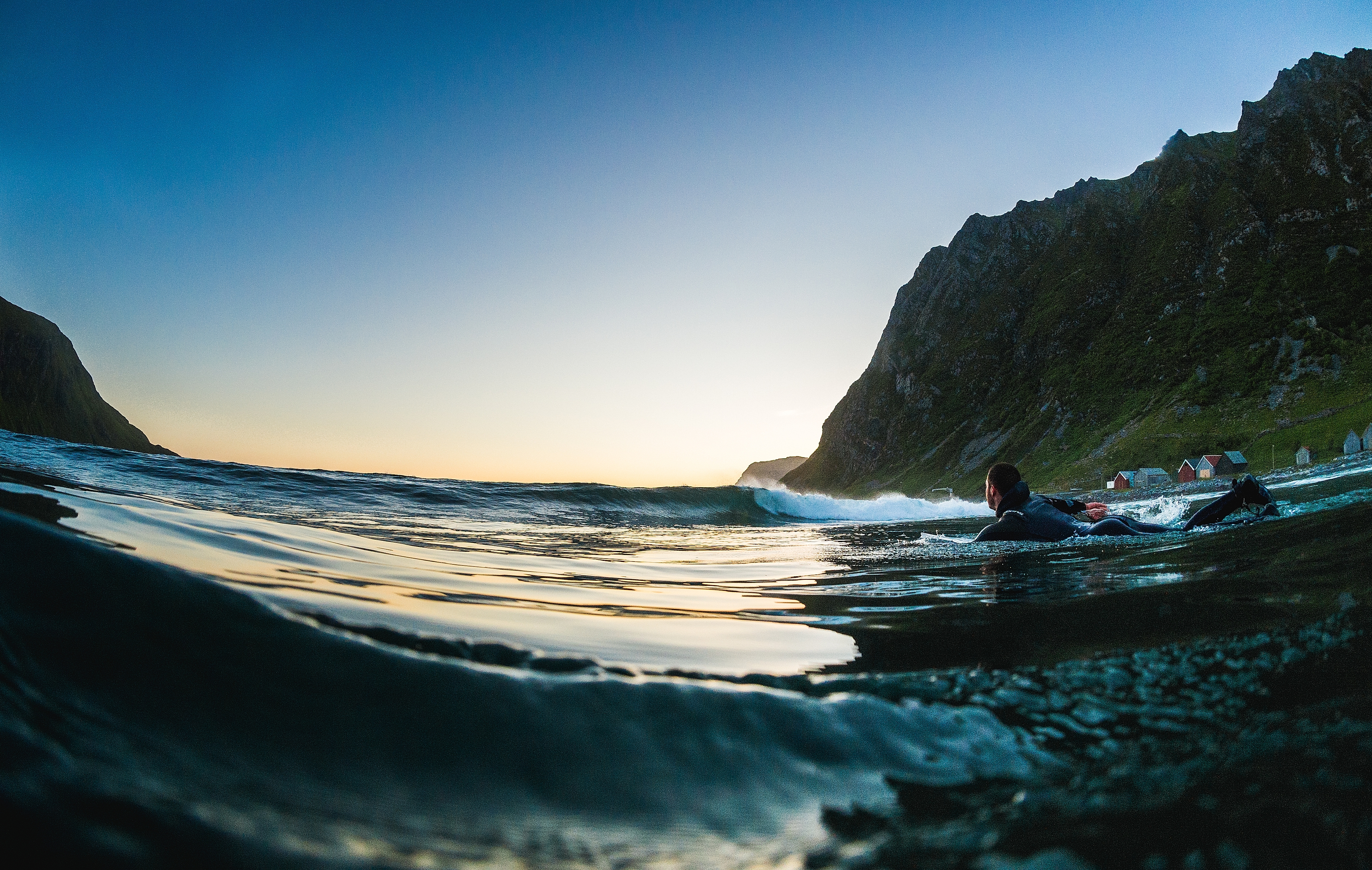 A man on lying on a surfboard swims towards the open sea at Hoddevik in Fjord Norway