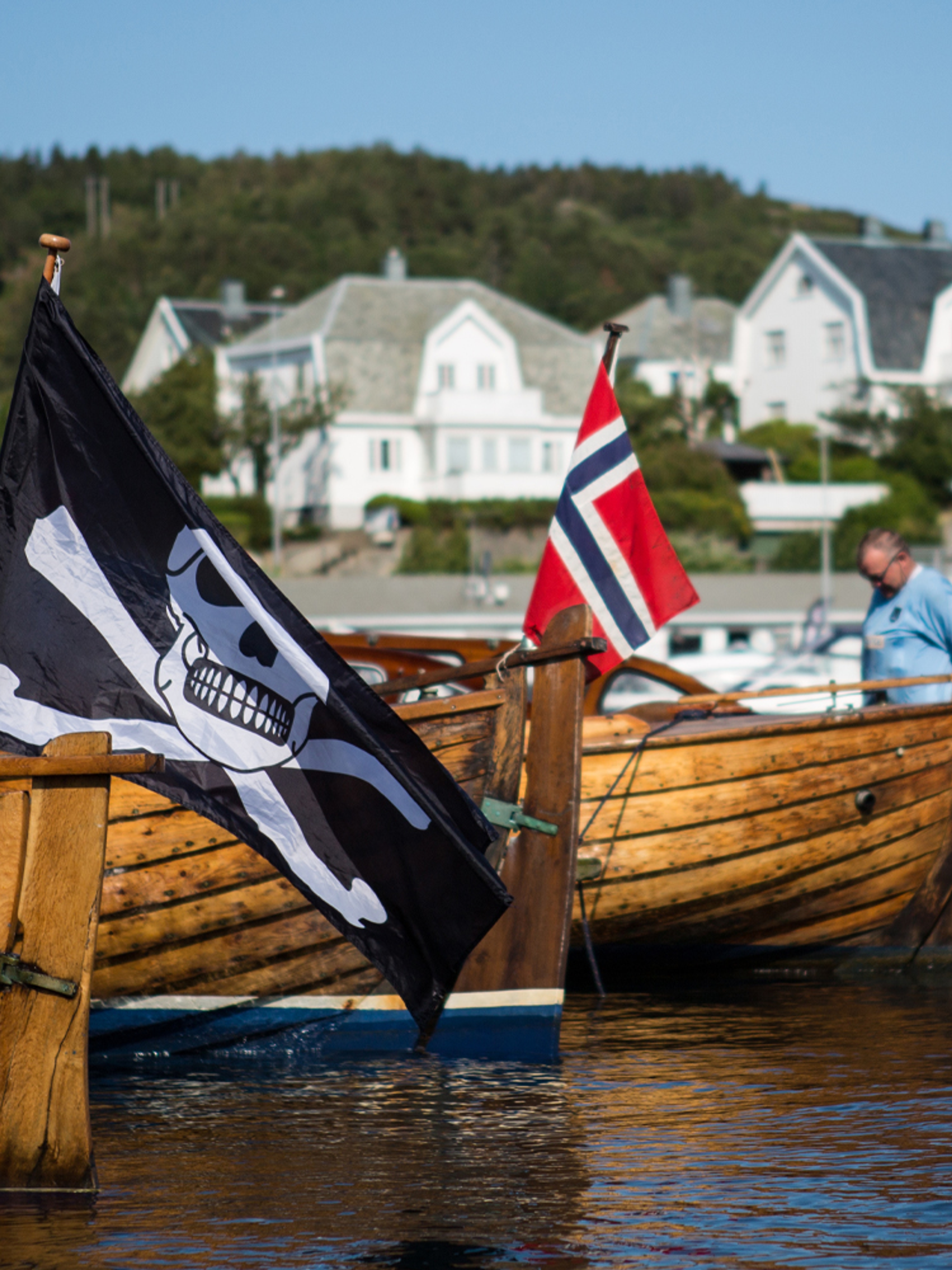 Wooden boats, one with a pirate flag, in Farsund, Southern Norway on a summer day.