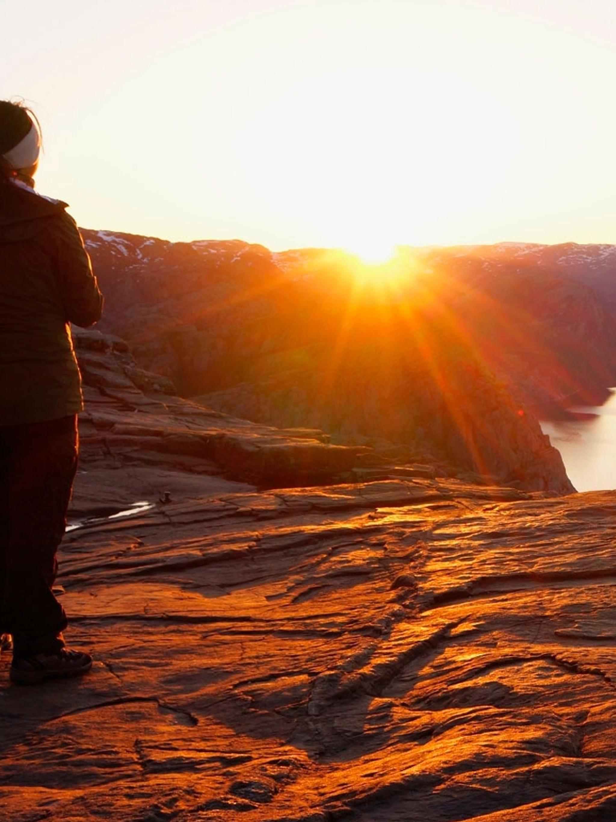En person ser på soloppgangen fra Preikestolen i Ryfylke i Norge