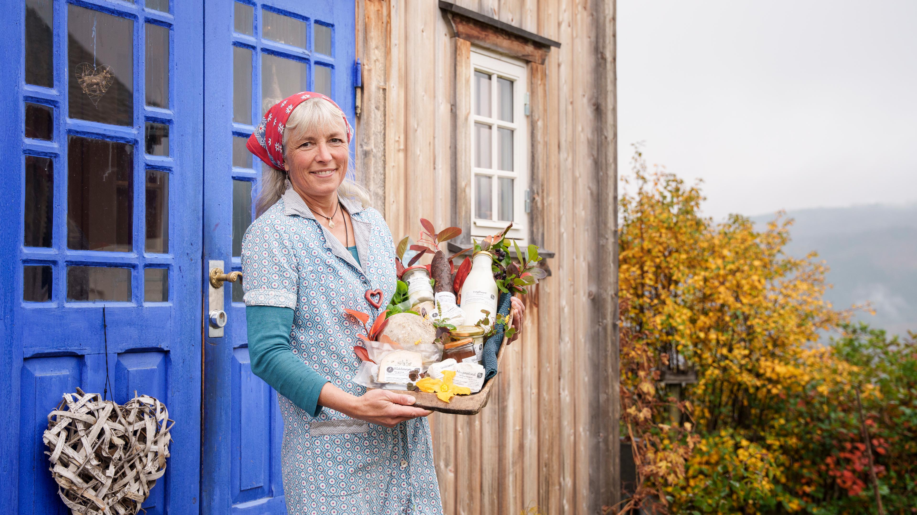 A woman holding a tray with local products outside of Nørrestogo farm in Valdres.