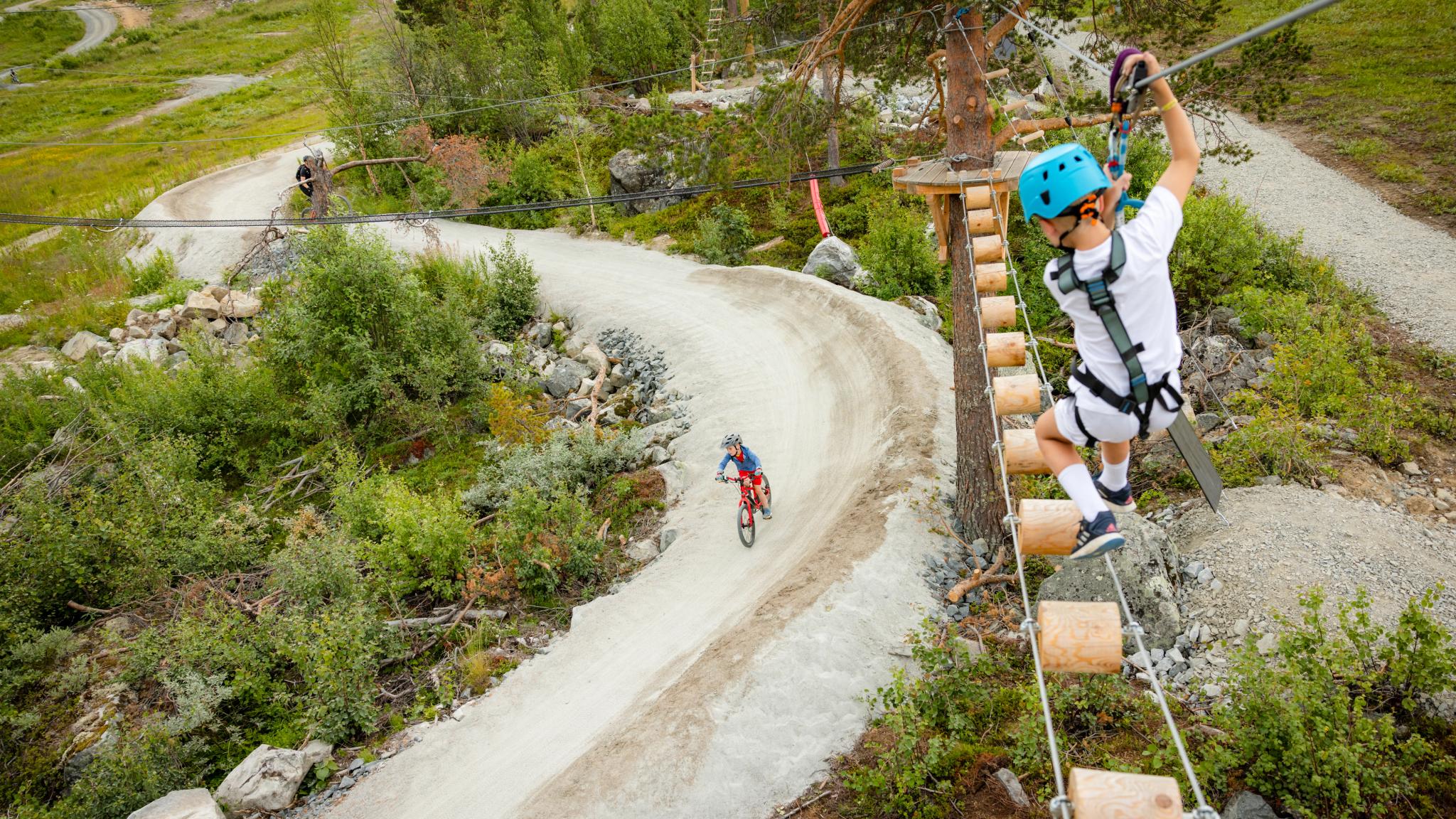 One child biking and one child climbing in Gelo Høyt og Lavt High Rope Course
