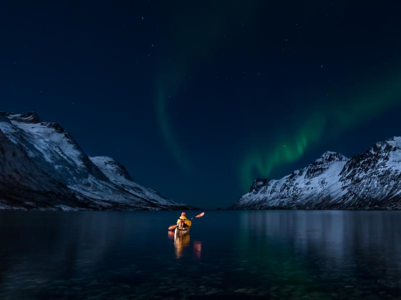 A woman paddling under the northern lights in Lofoten, Northern Norway