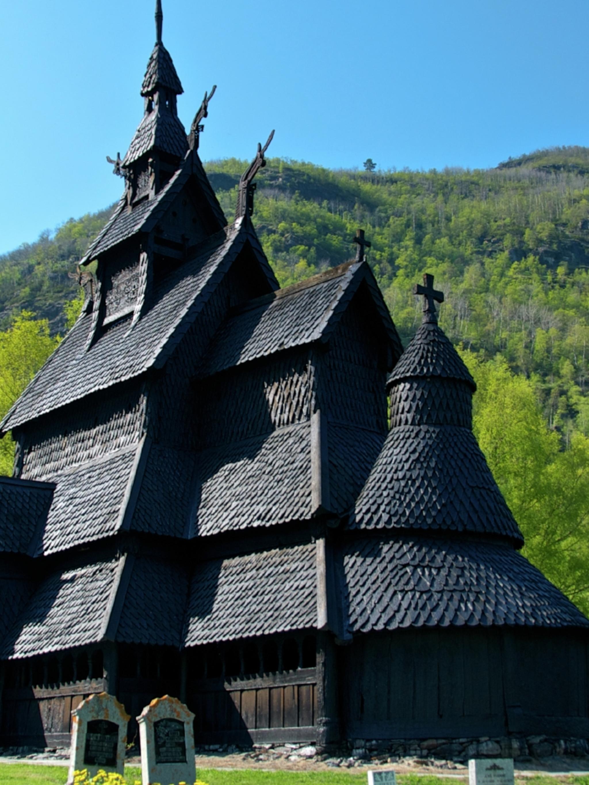 Borgund stave church with headstones in front and trees and hills in the back
