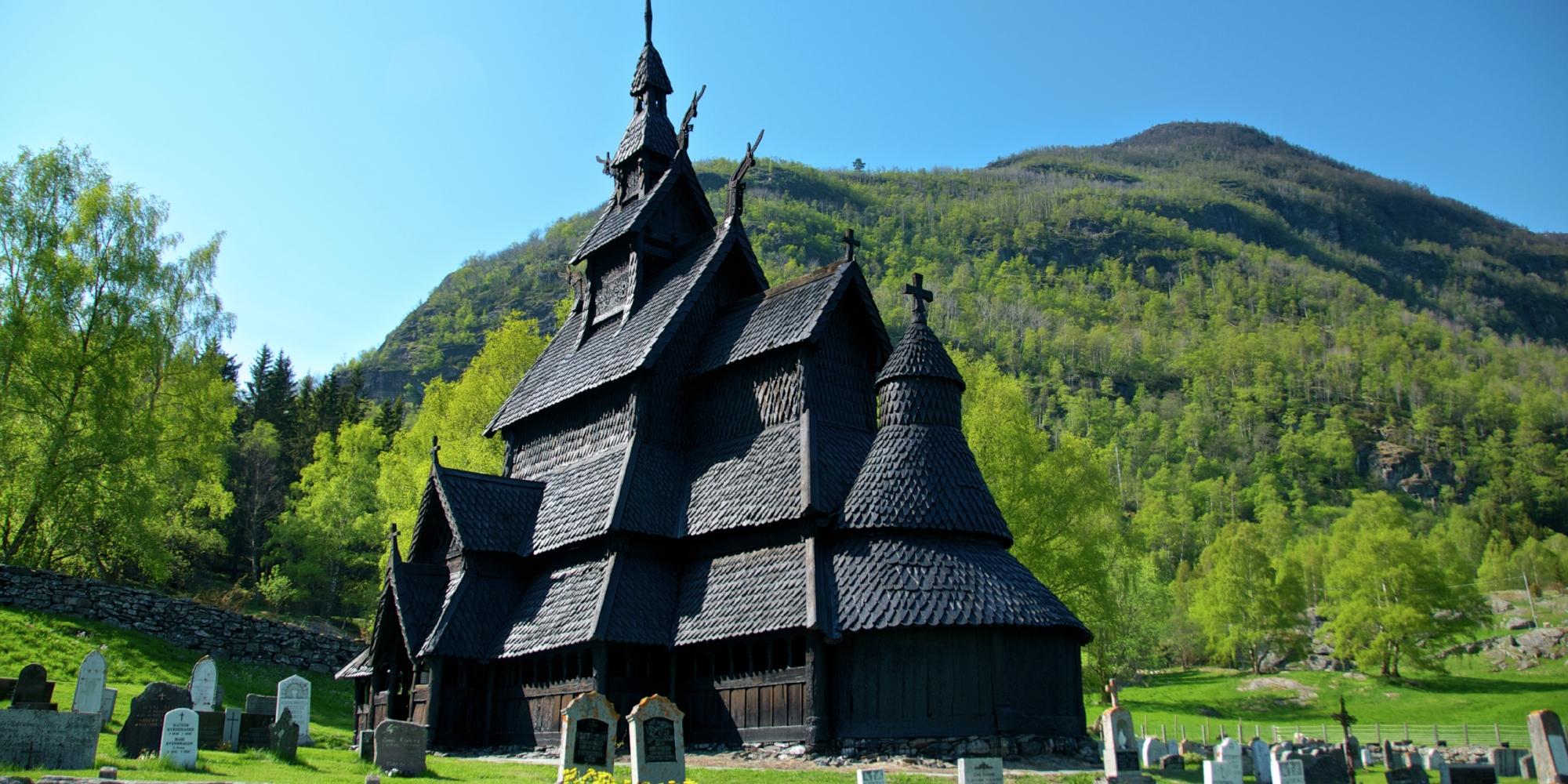 Borgund stave church with headstones in front and trees and hills in the back