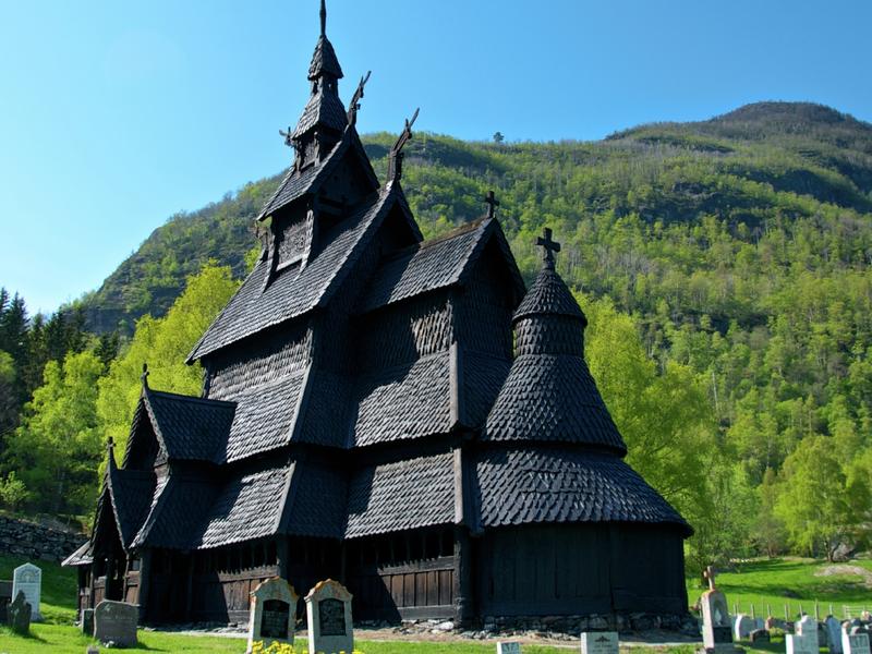 Borgund stave church with headstones in front and trees and hills in the back