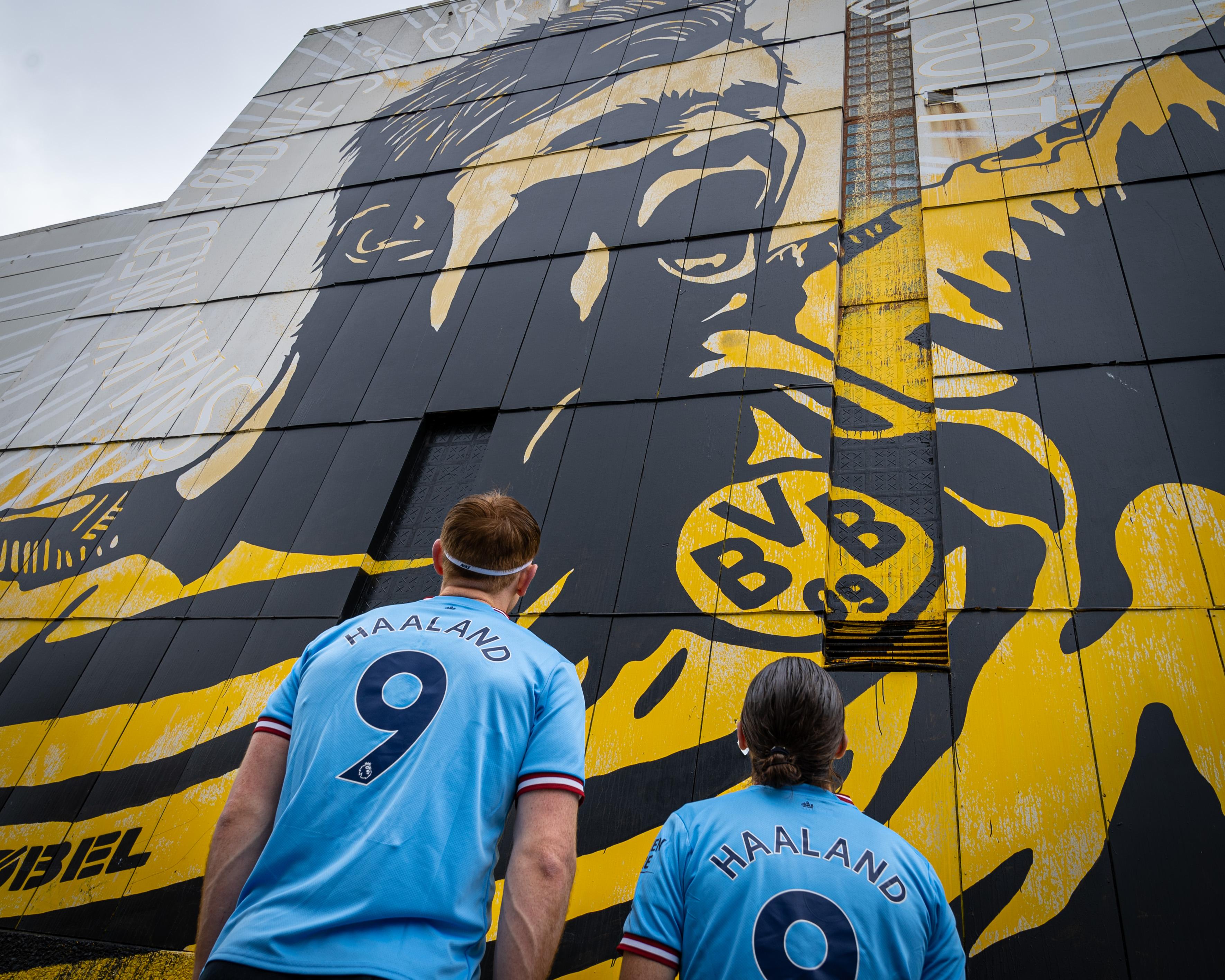 Two men looking the street art of Erling Braut Haaland by Pøbel in Bryne, Fjord Norway