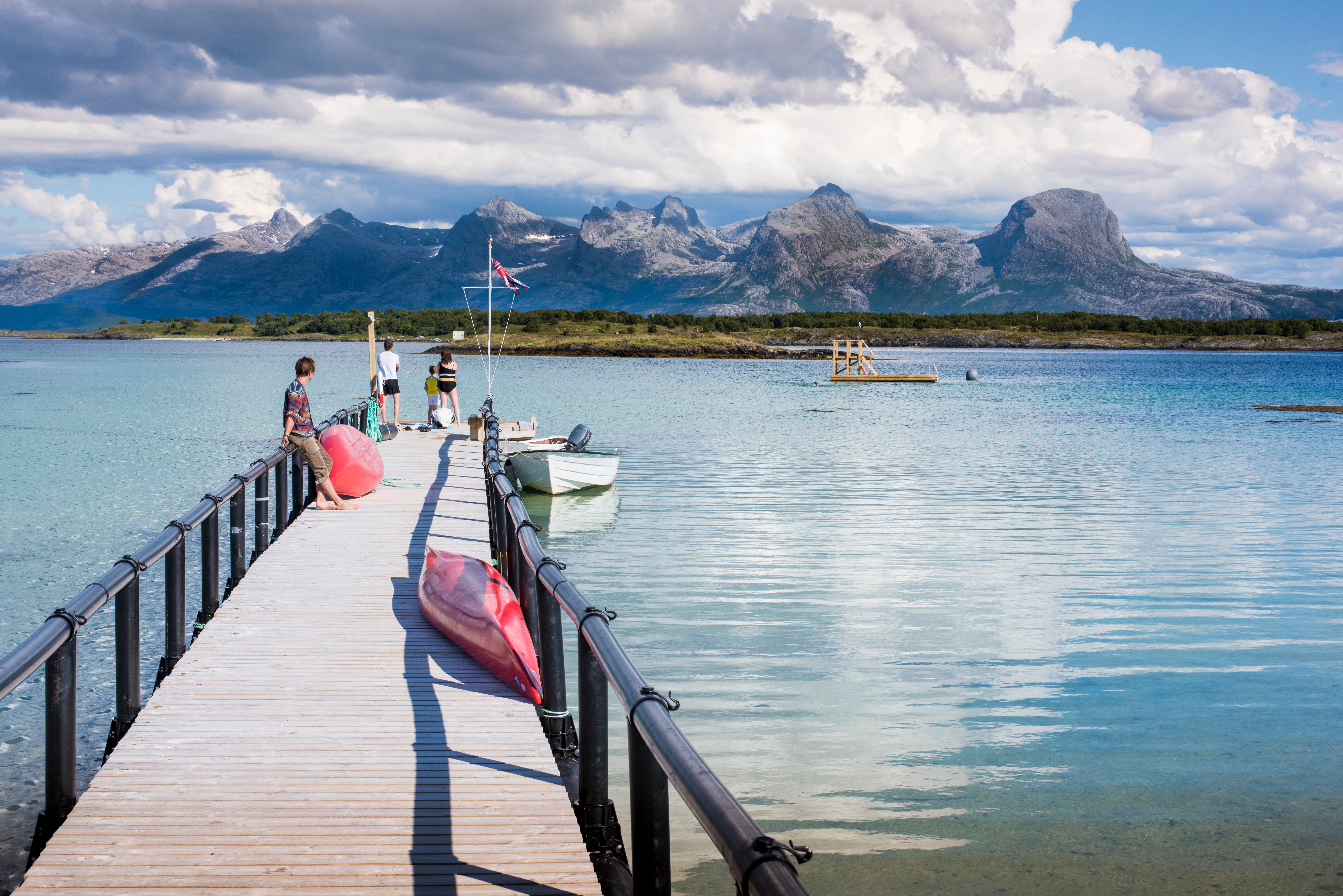 People standing along a pier in Helgeland, Northern Norway. In the background: The Seven Sisters mountain range.