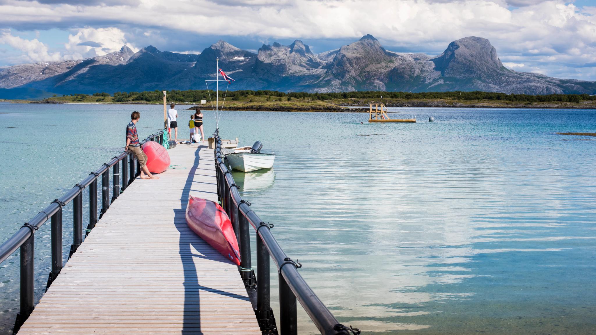 People standing along a pier in Helgeland, Northern Norway. In the background: The Seven Sisters mountain range.