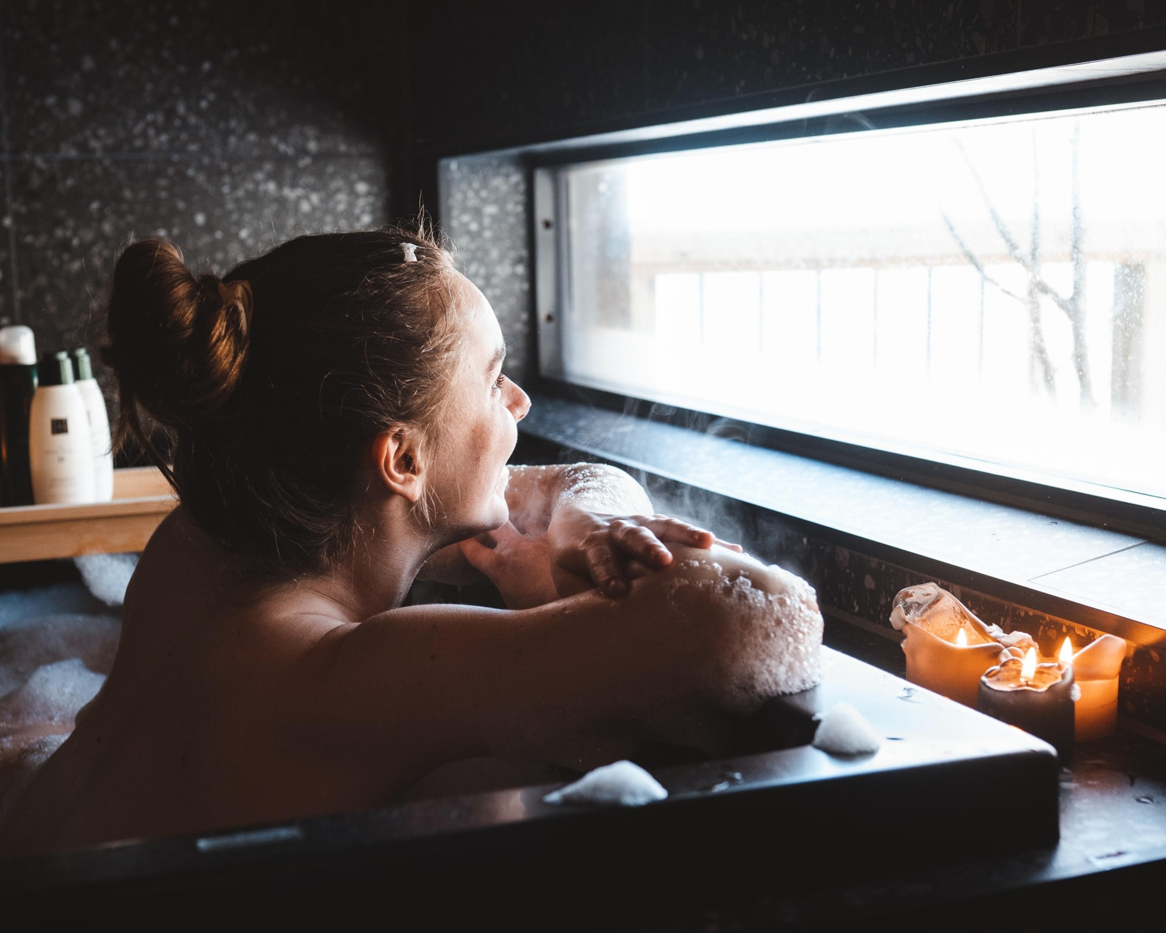 A woman bathing while looking out of the window.