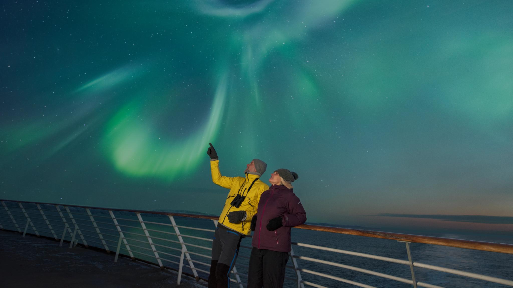 Two people on the deck of a Hurtigruten ship under the norhtern lights in Northern Norway